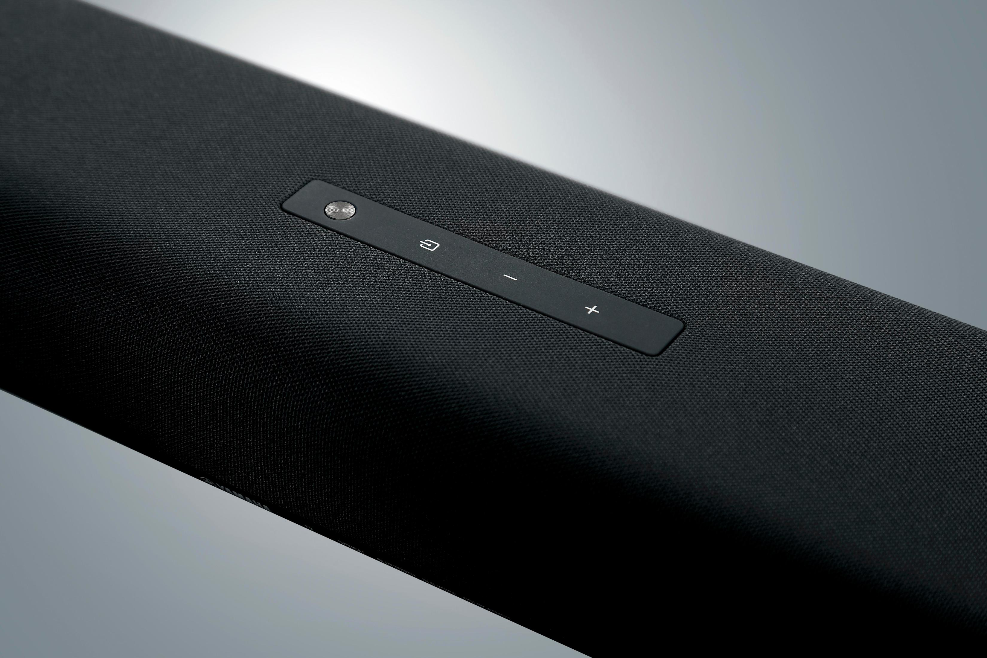 Black soundbar with volume and power buttons on a grey background, close-up shot.