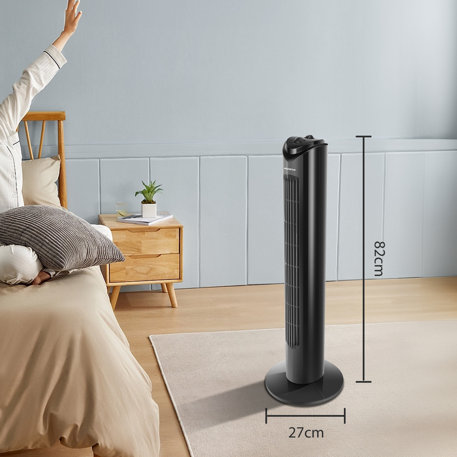 Ventilador negro alto junto a una cama. Una persona levanta la mano.
