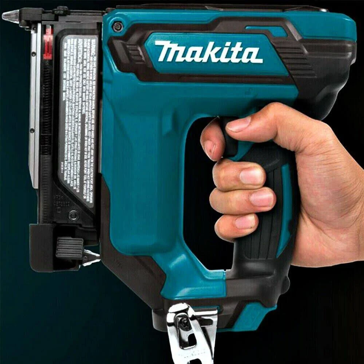 Hand hält eine türkisblaue Makita-Nagelpistole. Schwarzer Griff, weißes Logo. Dunkler Hintergrund.