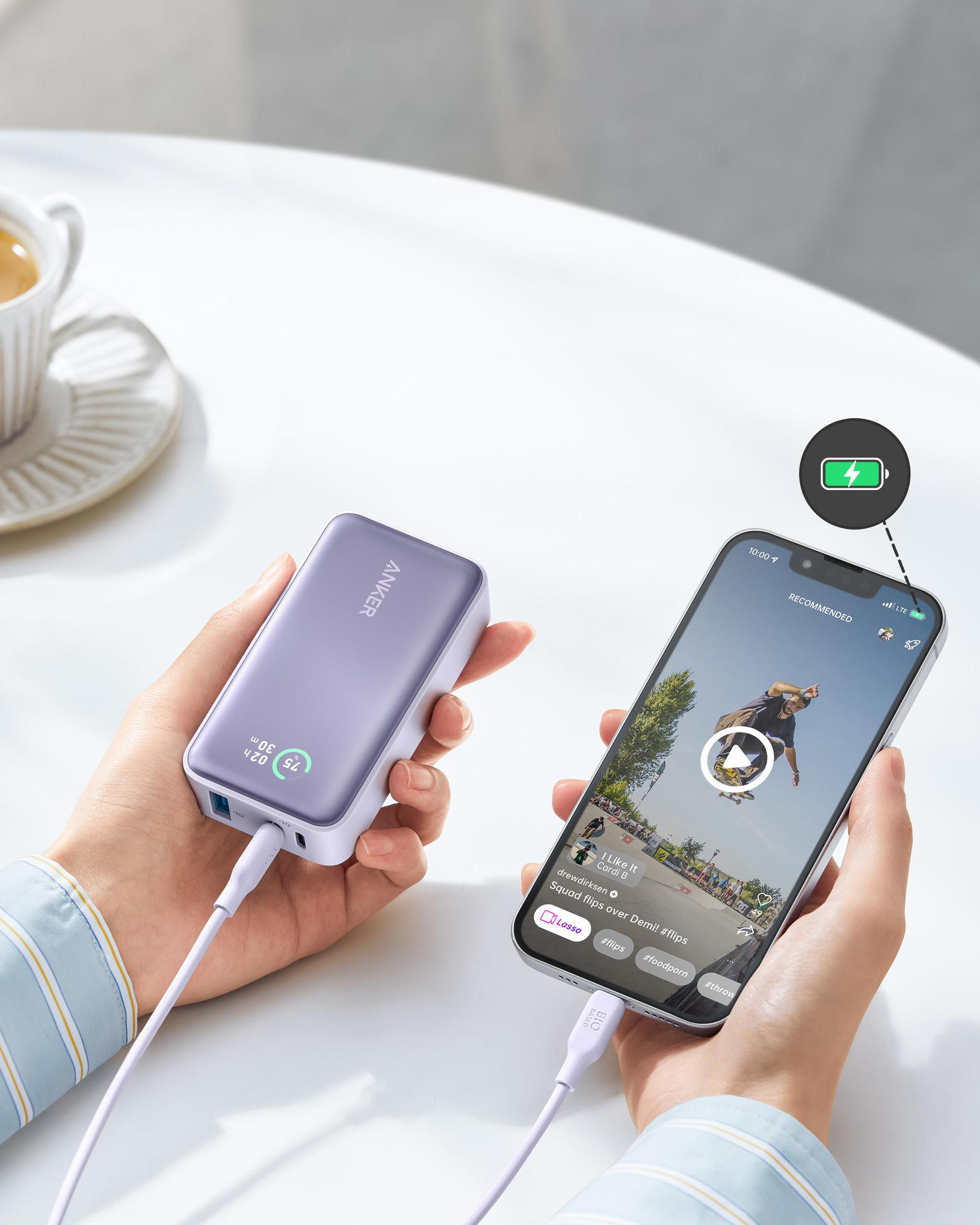 Una persona tiene in mano un power bank viola e un telefono che mostra un video.