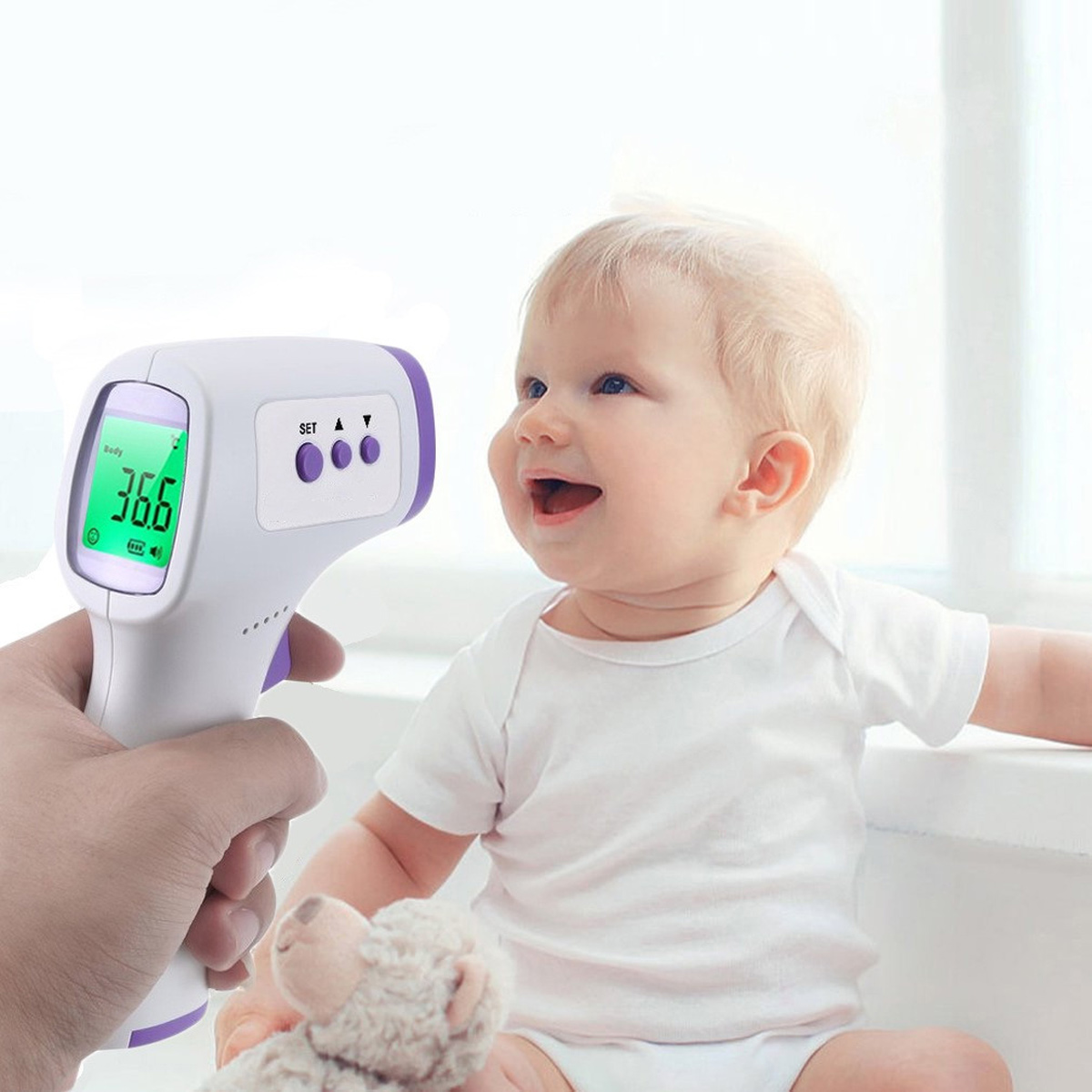 Baby mit fröhlichem Gesichtsausdruck, Temperaturmessung mit kontaktlosem Thermometer. Anzeige zeigt 36,6.