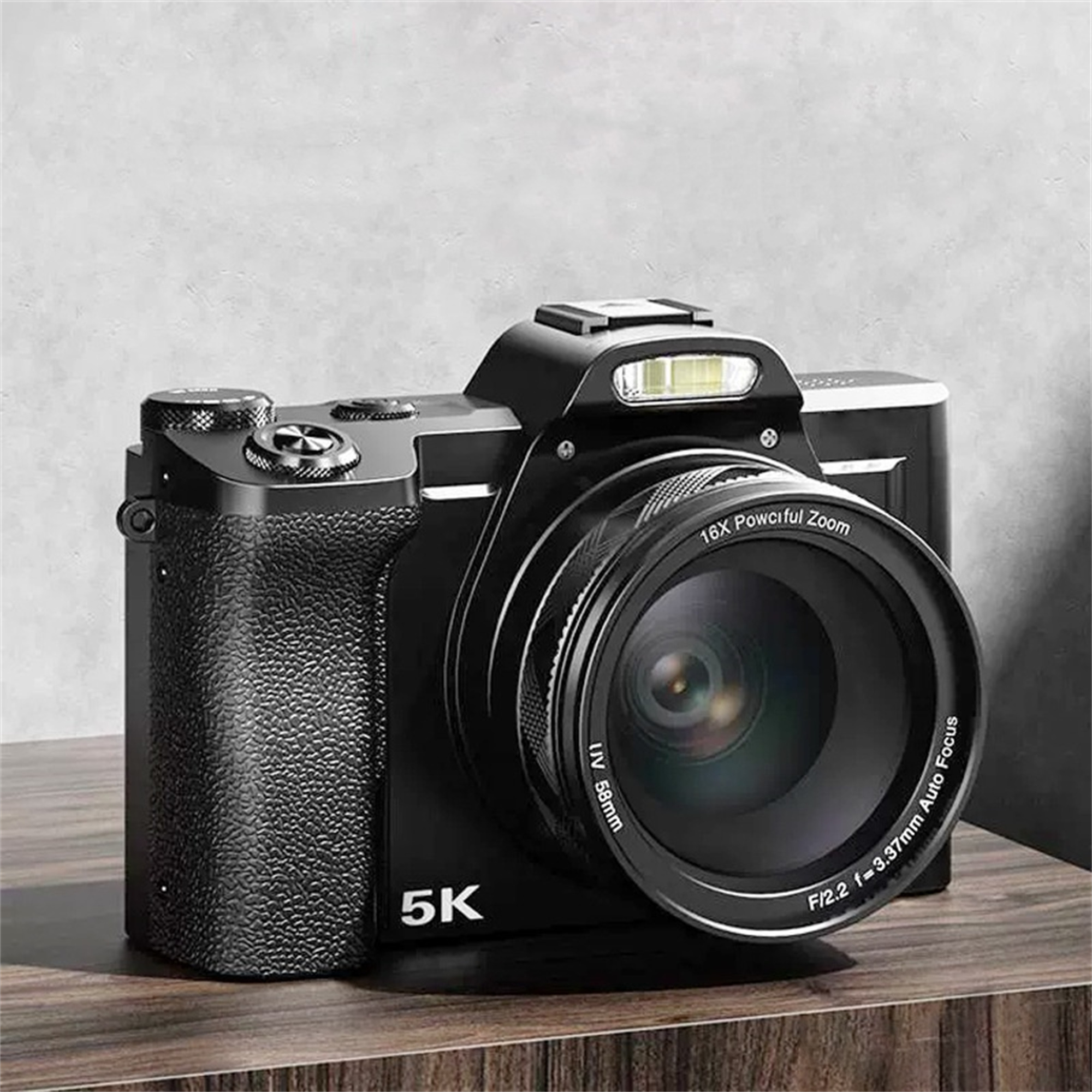 Eine schwarze Kamera mit großem Objektiv, die auf einer Holzoberfläche steht. Der Zoom ist mit 16X markiert.