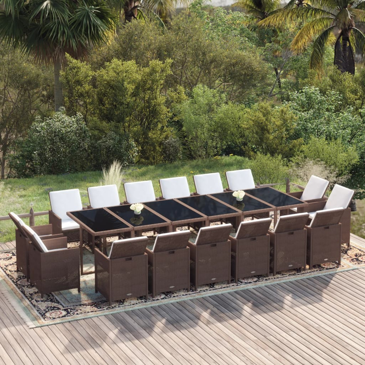 Essgruppe im Freien mit großem Tisch und Stühlen auf einer Terrasse, mit Bäumen und Holzzaun im Hintergrund.