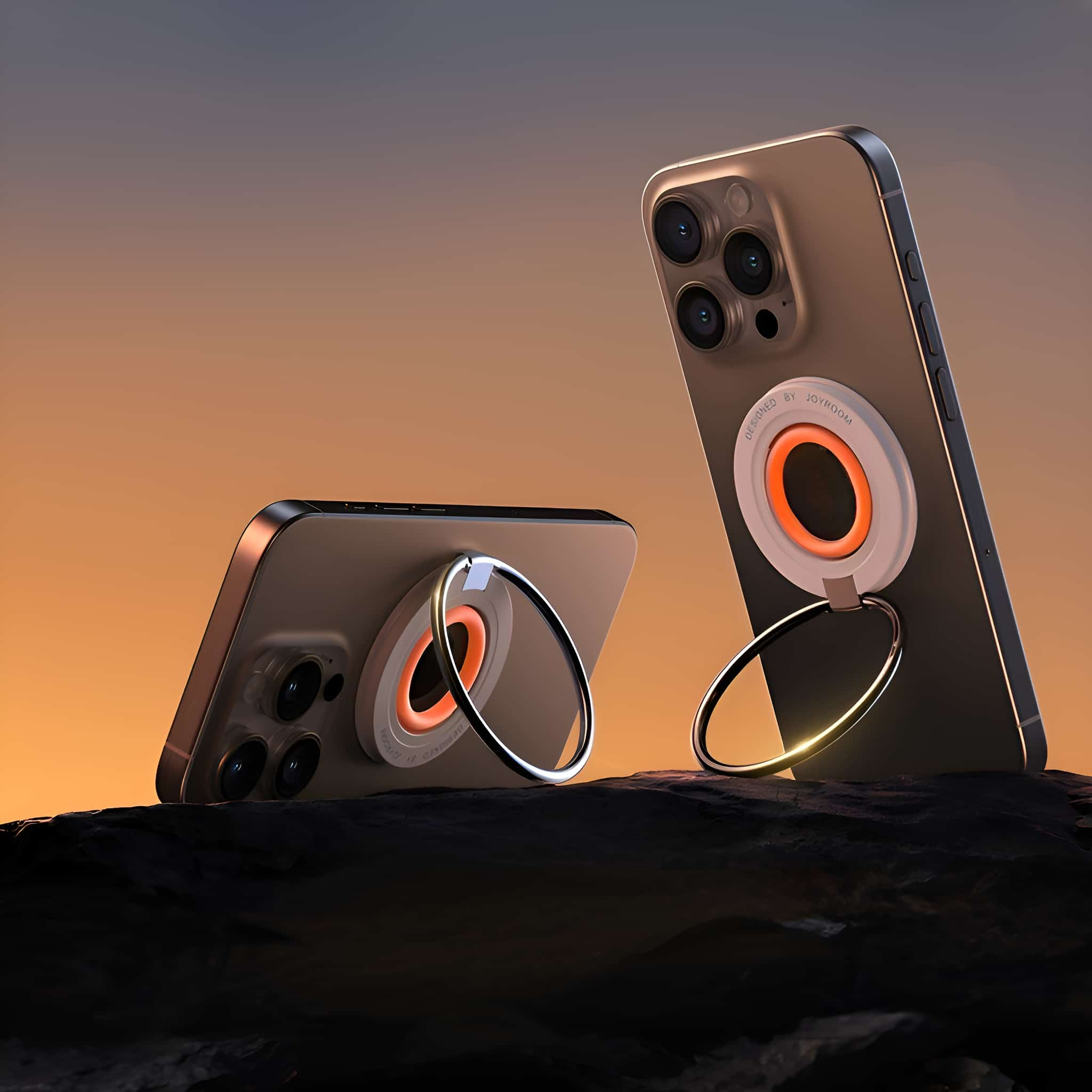 Zwei Smartphones mit Ringhaltern auf dunkler Oberfläche, mit Sonnenuntergang im Hintergrund.