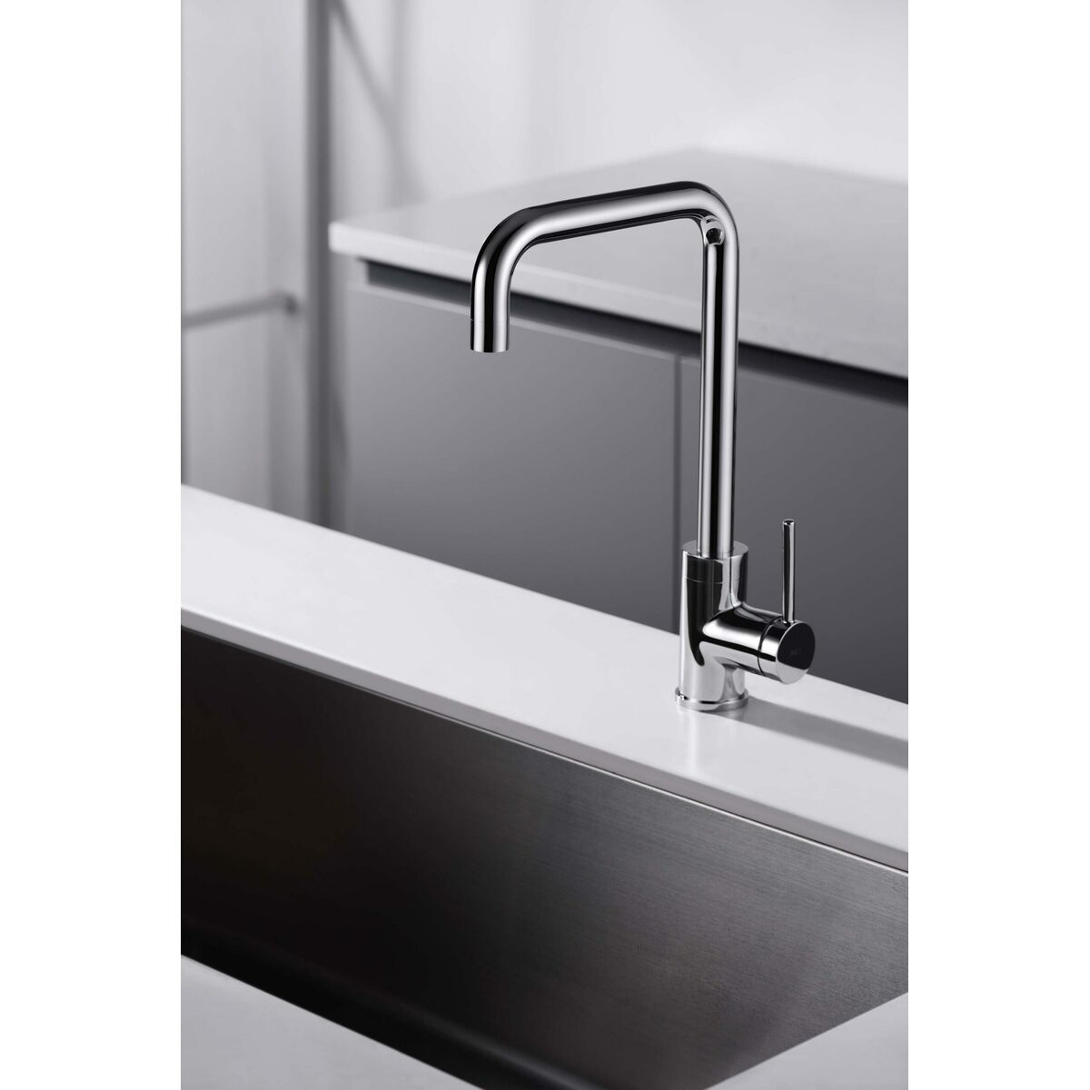 Rubinetto cromato con una leva singola. È installato su un piano bianco. Lavello in acciaio inox.