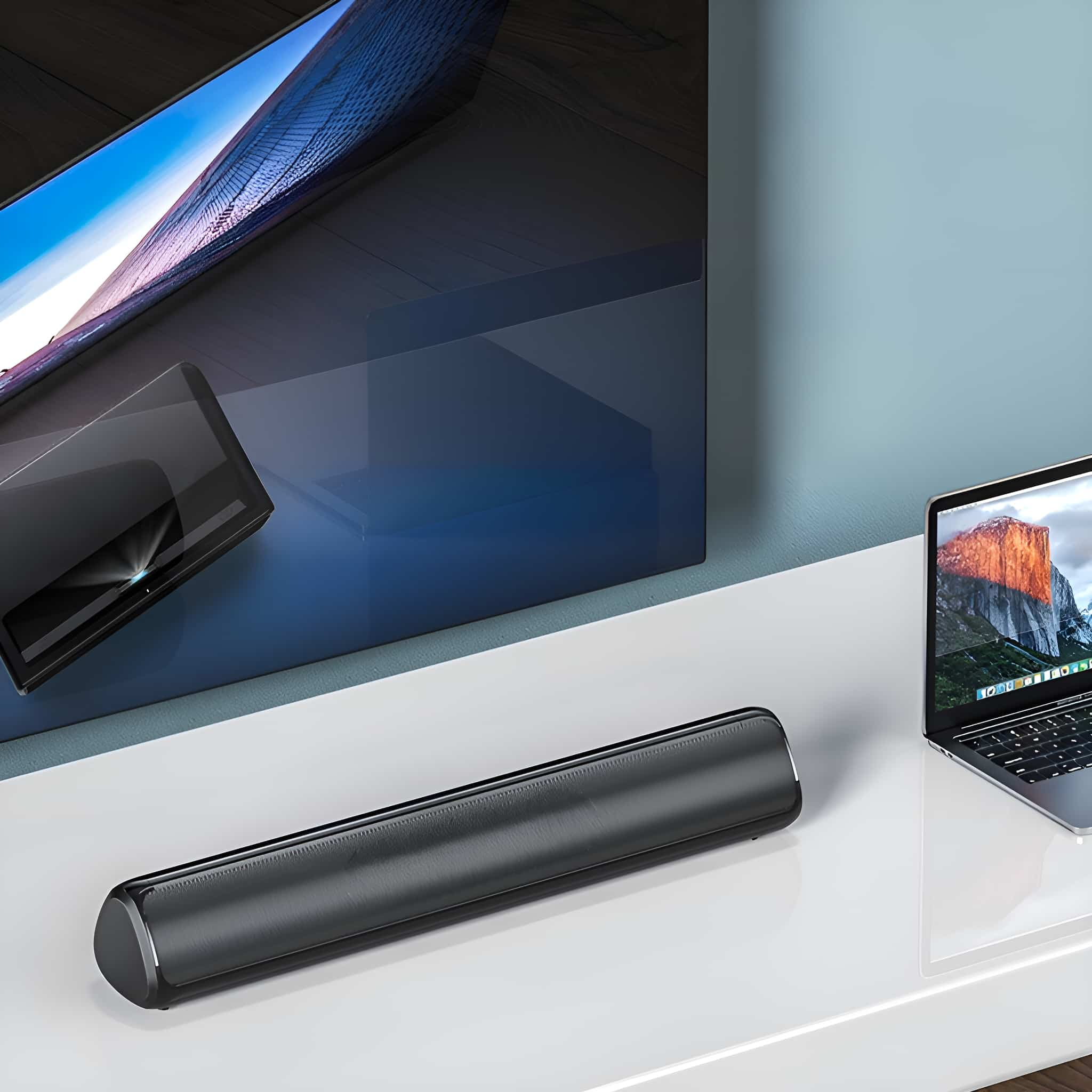 Eine Soundbar auf weißer Oberfläche, neben TV und Laptop.