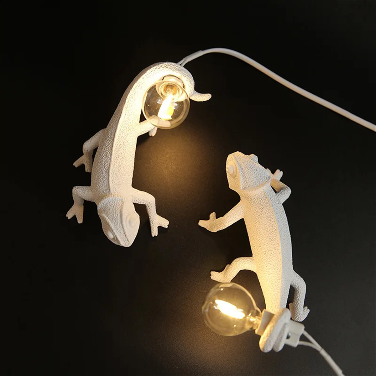 Zwei weiße Eidechsen-Lichter mit Glühbirnen. Sie befinden sich auf einer schwarzen Oberfläche.