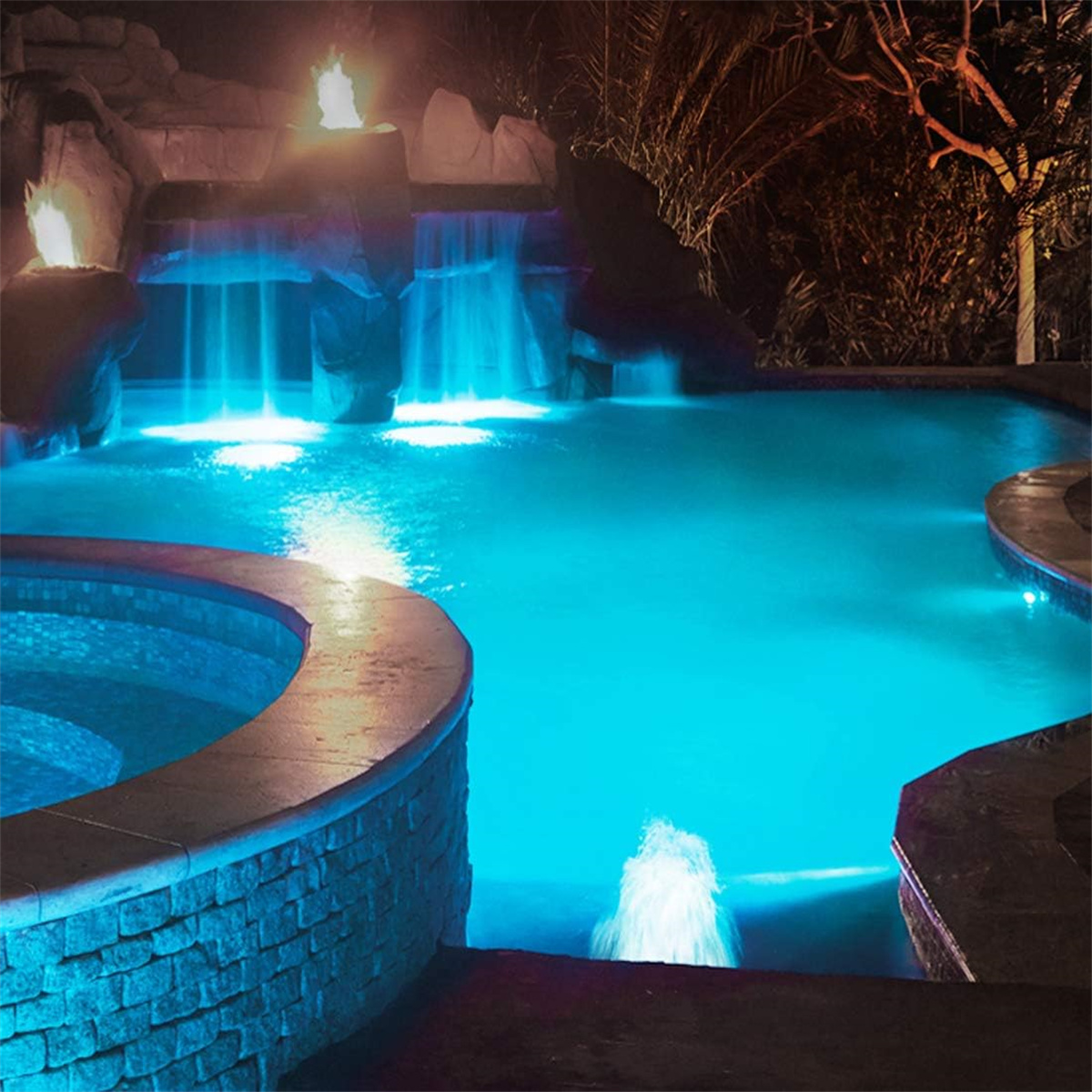 Nachtszenen-Pool mit blauen Lichtern und beleuchteten Wasserfällen, umgeben von Felsen.