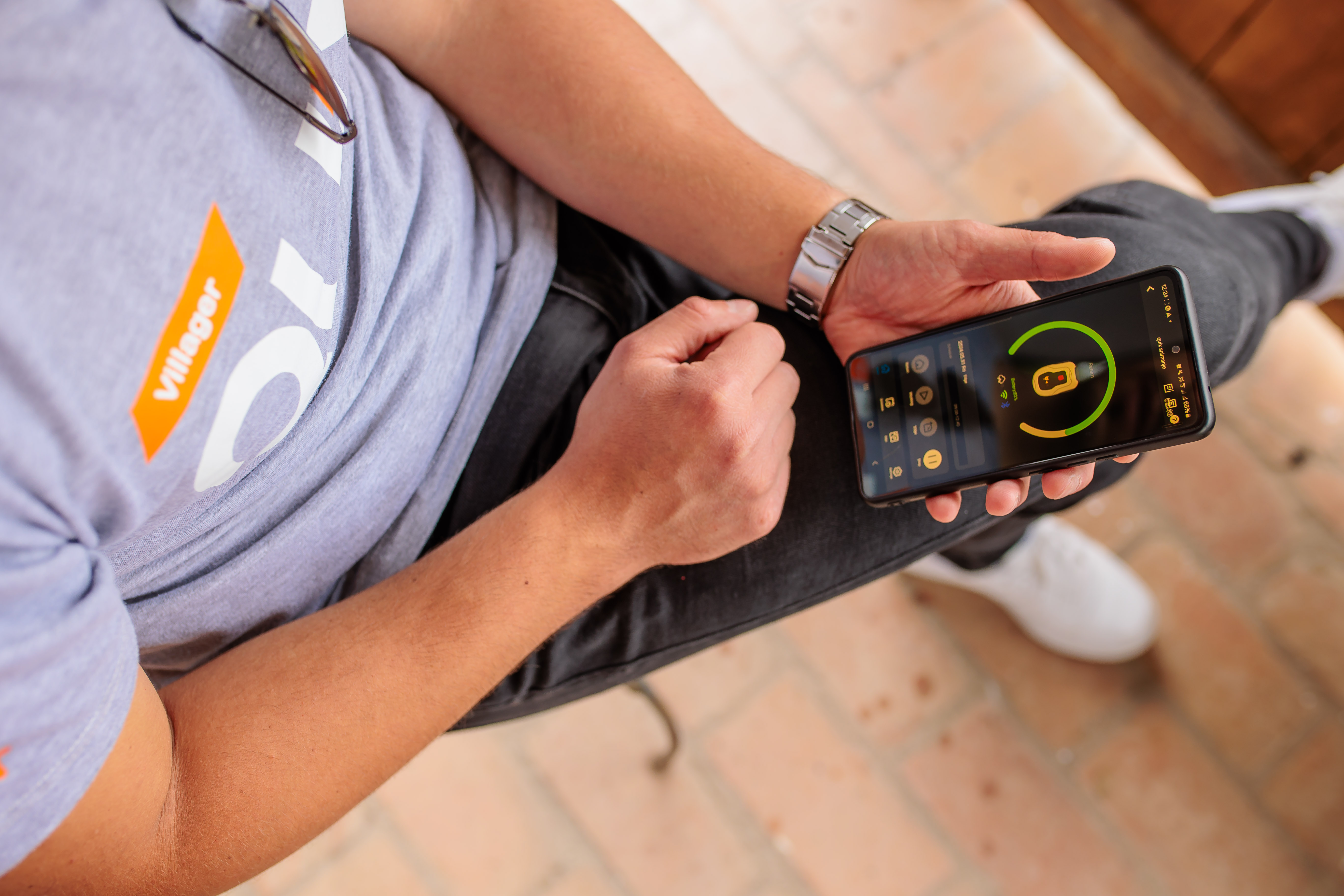 Person hält ein Smartphone, das eine App-Oberfläche anzeigt. Die Person trägt ein T-Shirt.