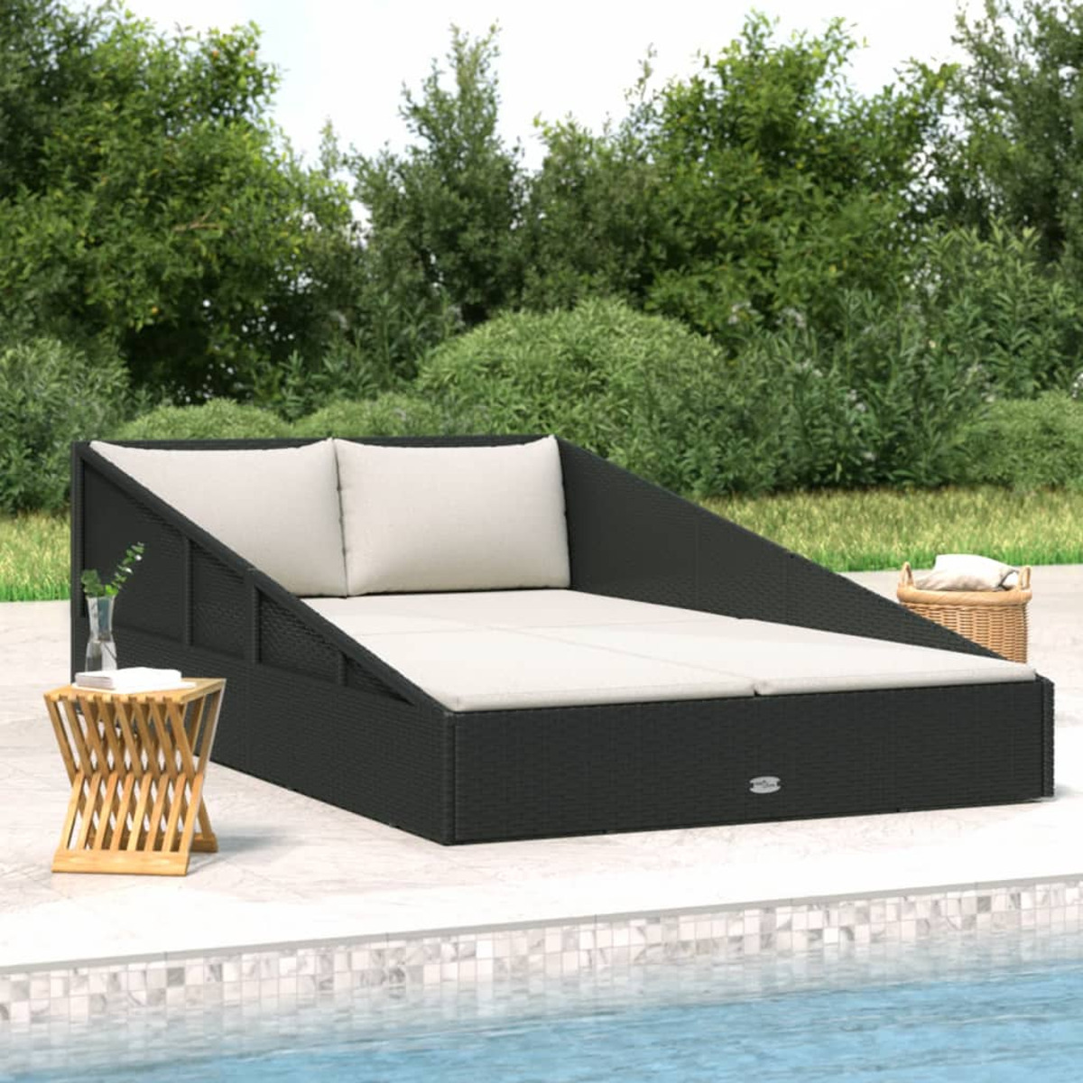 Schwarzes Rattan-Outdoor-Daybed mit zwei Kissen, einem kleinen Tisch und grünem Heckenhintergrund.