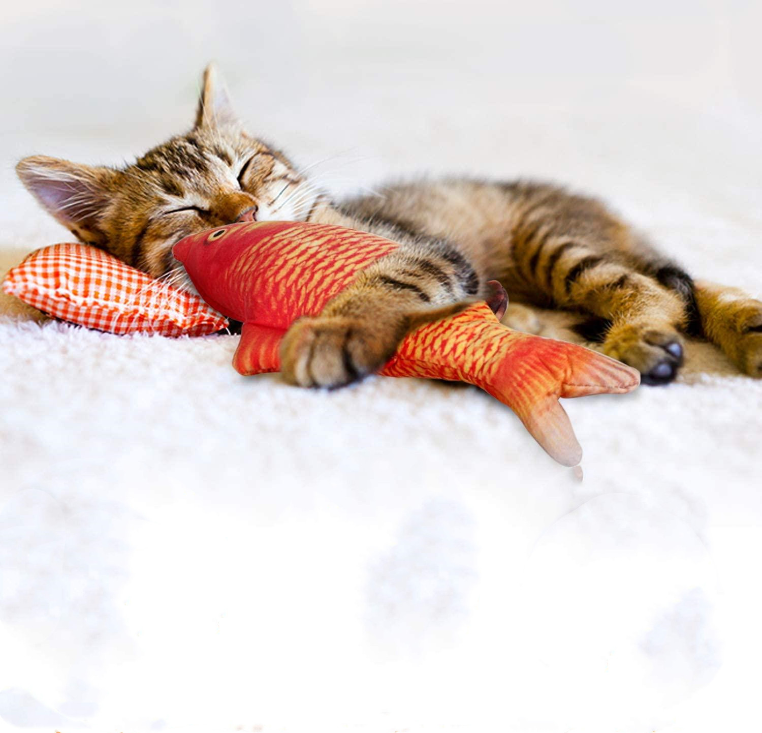 Schlafende getigerte Katze mit Spielzeugfisch auf weißer Decke.