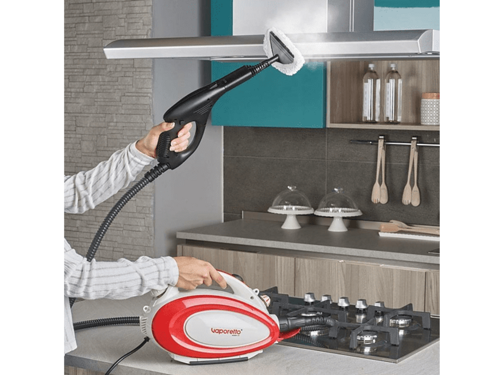 Osoba używająca parownicy. Urządzenie czerwono-białe, czarny uchwyt. Para nad kuchenką.