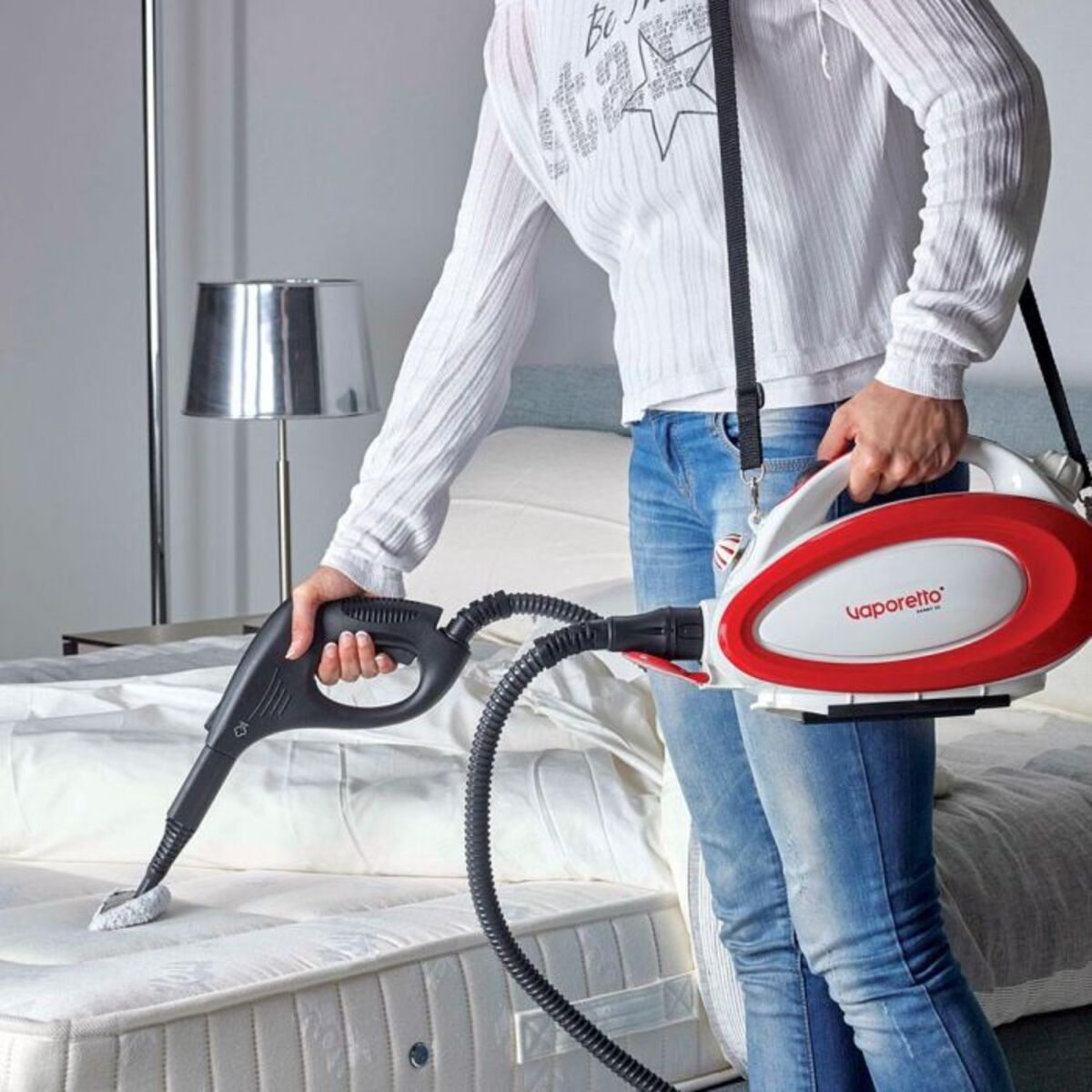 Osoba czyszcząca materac parownicą. Czyszczący jest czerwony i biały.
