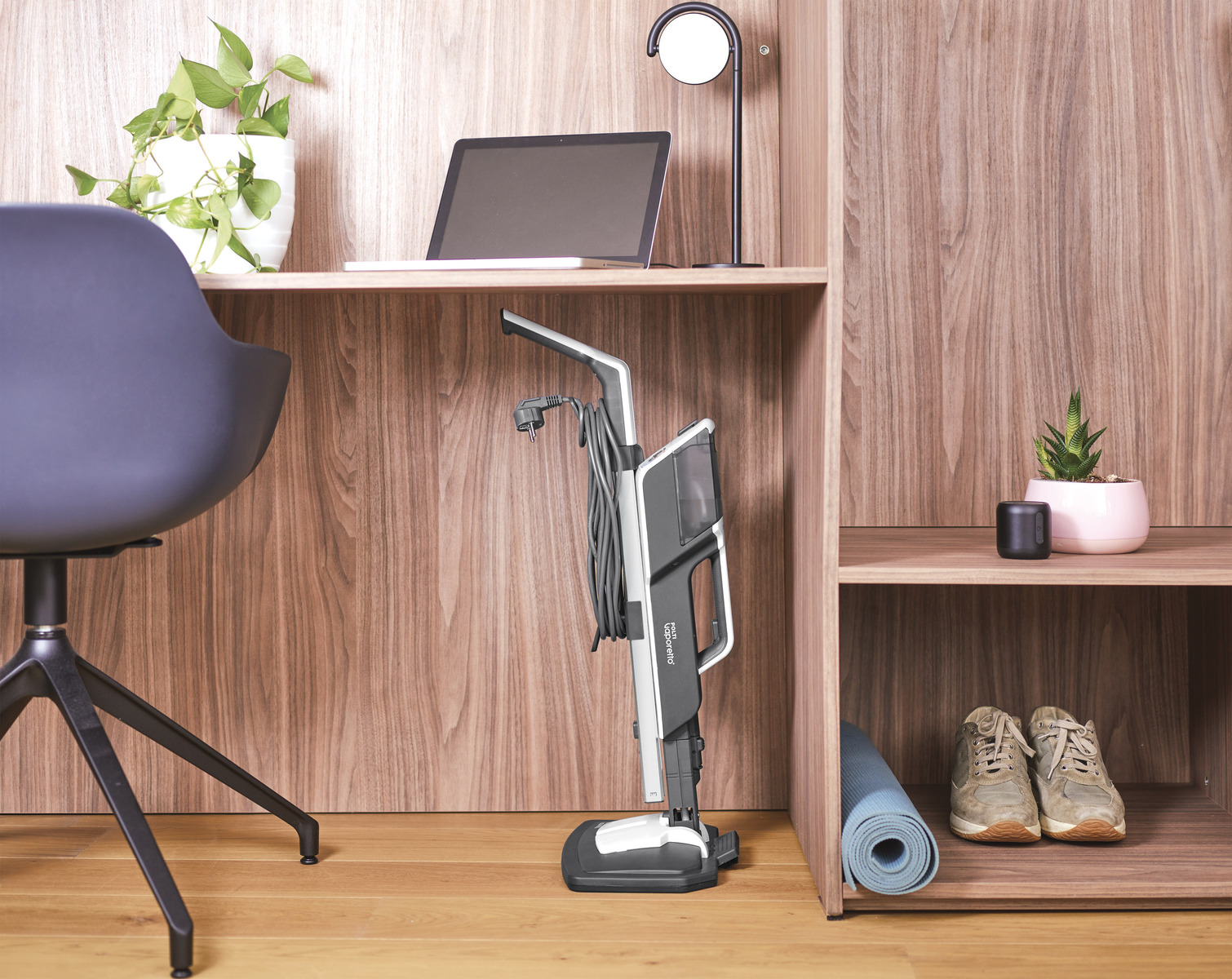 Składany odkurzacz jest przechowywany w drewnianej szafce, obok laptopa i rośliny.