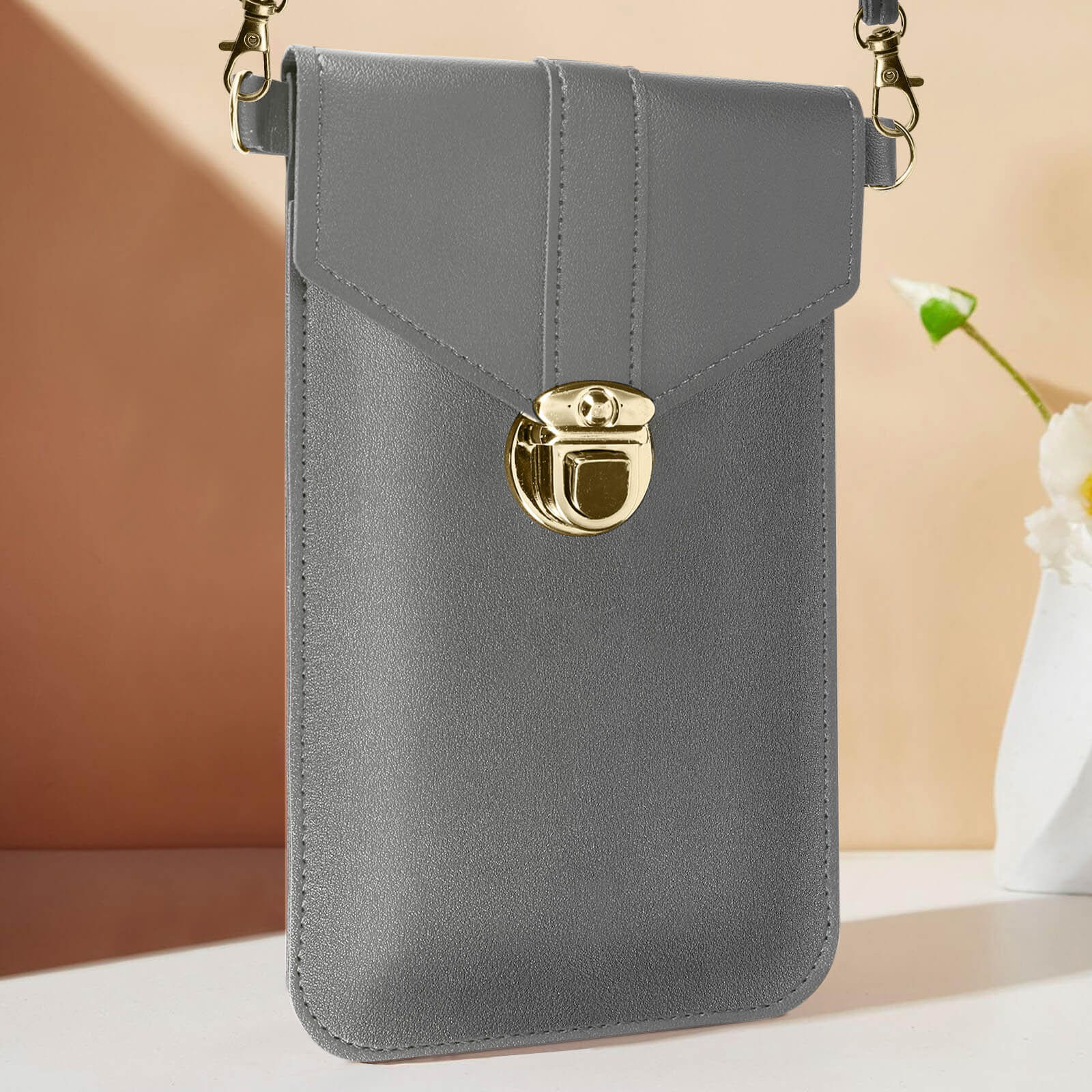 Un support de téléphone rectangulaire gris avec fermoir doré et chaîne.