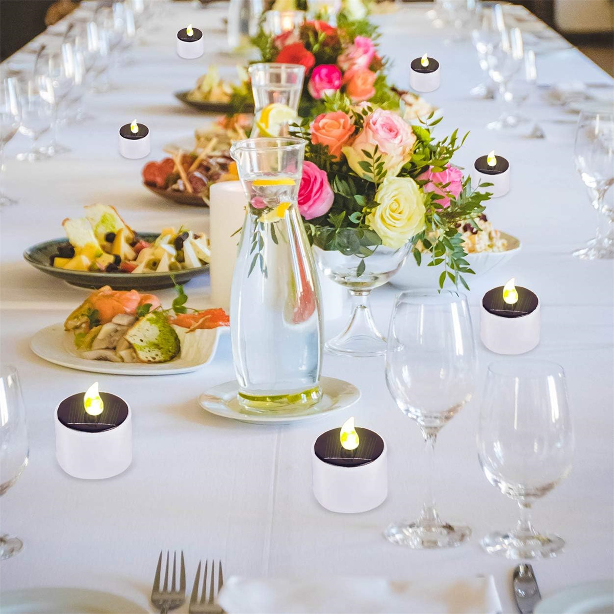 Tisch mit weißen Kerzen, Blumen, Gläsern und Essen. Eine weiße Tischdecke.