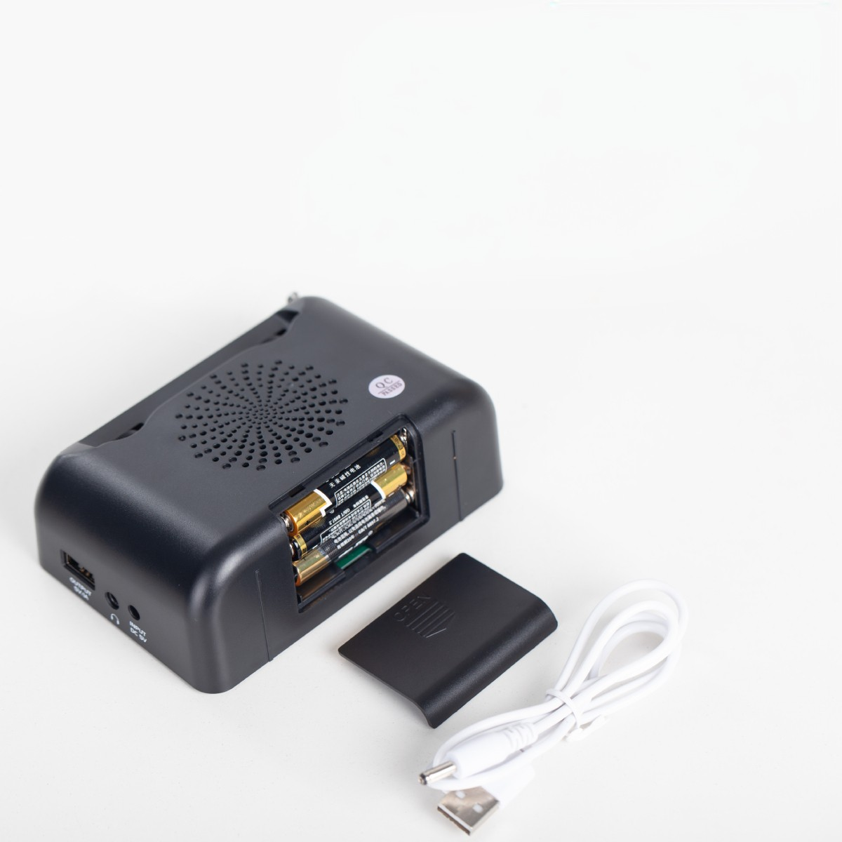Schwarzer tragbarer Lautsprecher mit Batterien und USB-Kabel. Das Batteriefach ist geöffnet. Weißer Hintergrund.