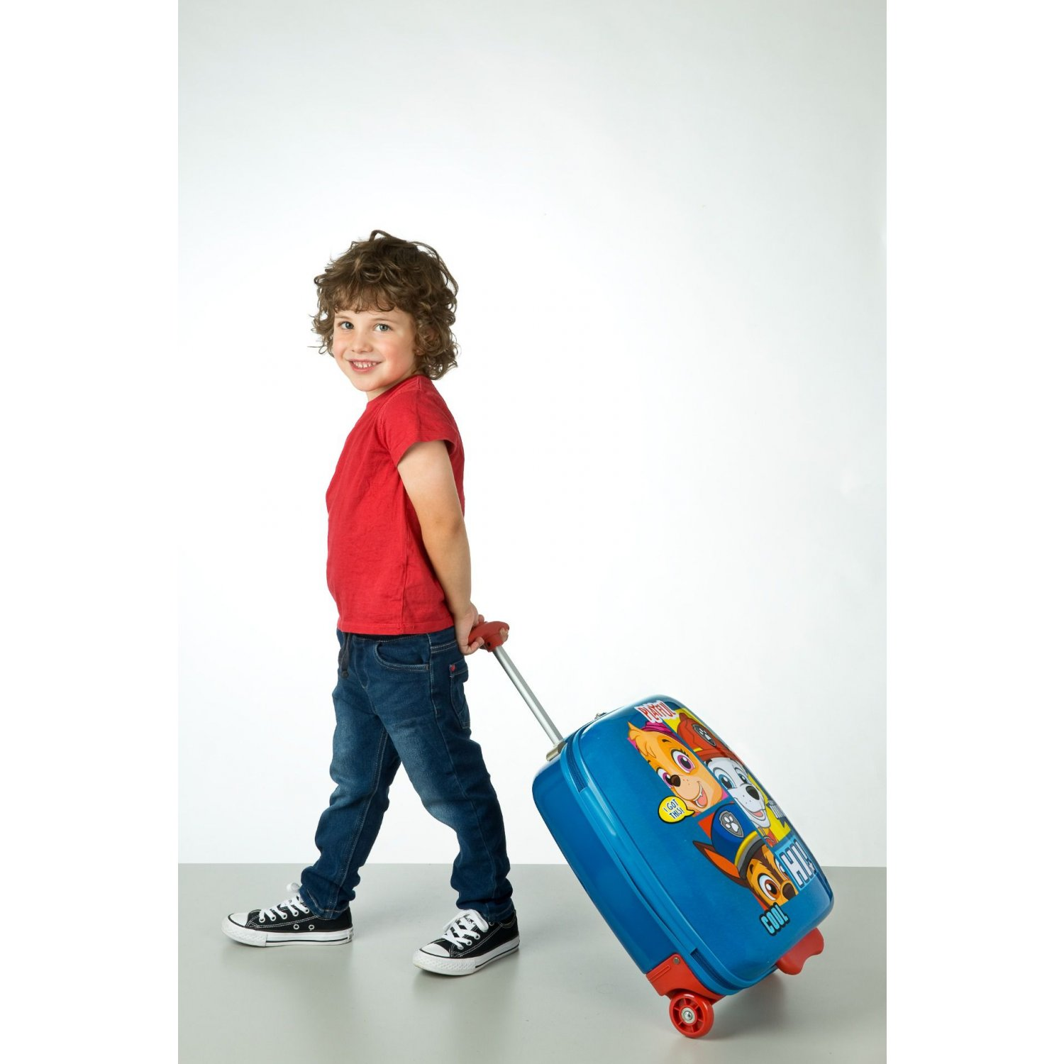 Ein junger Junge in rotem Hemd und Jeans zieht einen blauen Paw Patrol-Koffer.
