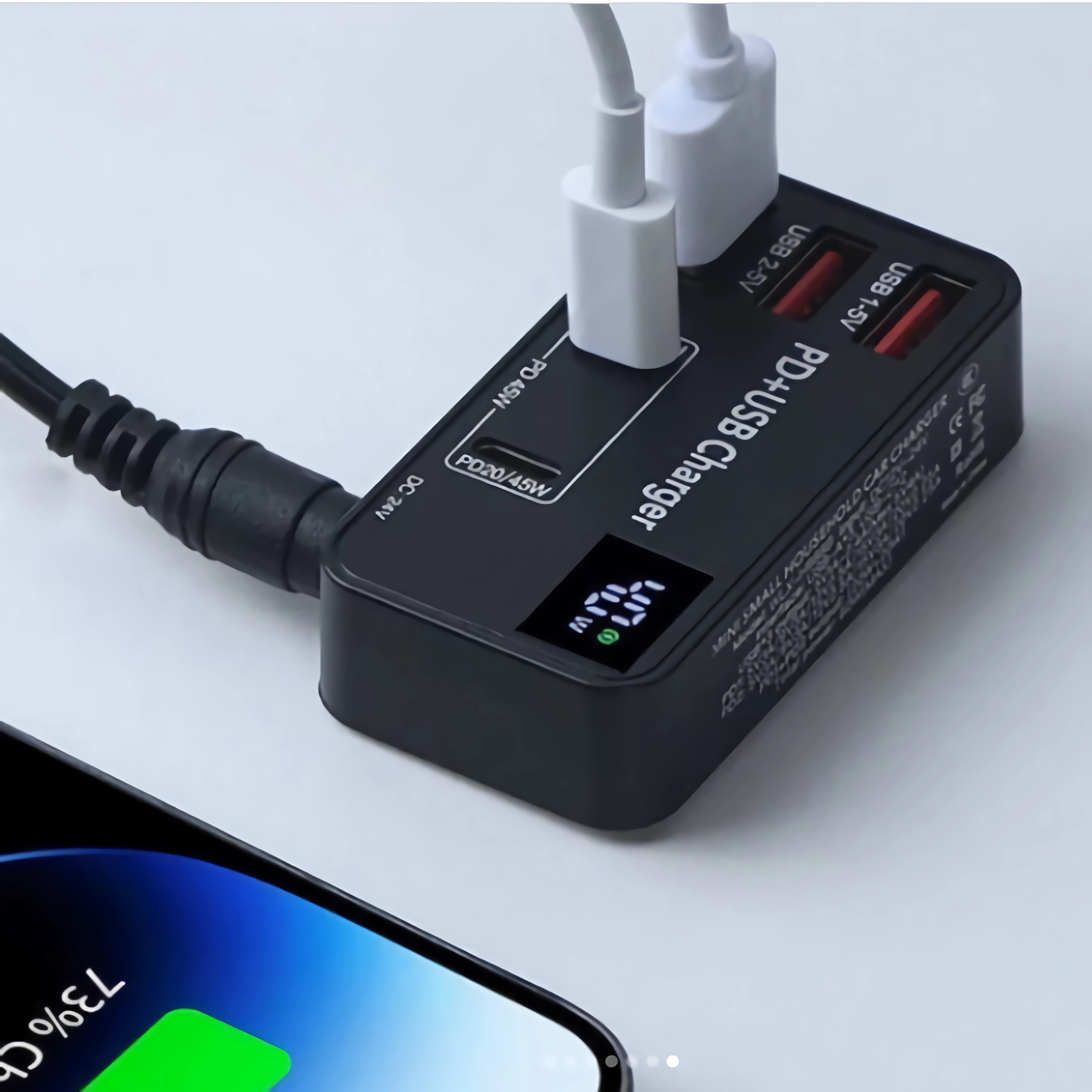 Ein schwarzes PD+USB-Ladegerät mit digitaler Anzeige, die 73 % Akku anzeigt. Weißer Hintergrund mit einem Telefon.