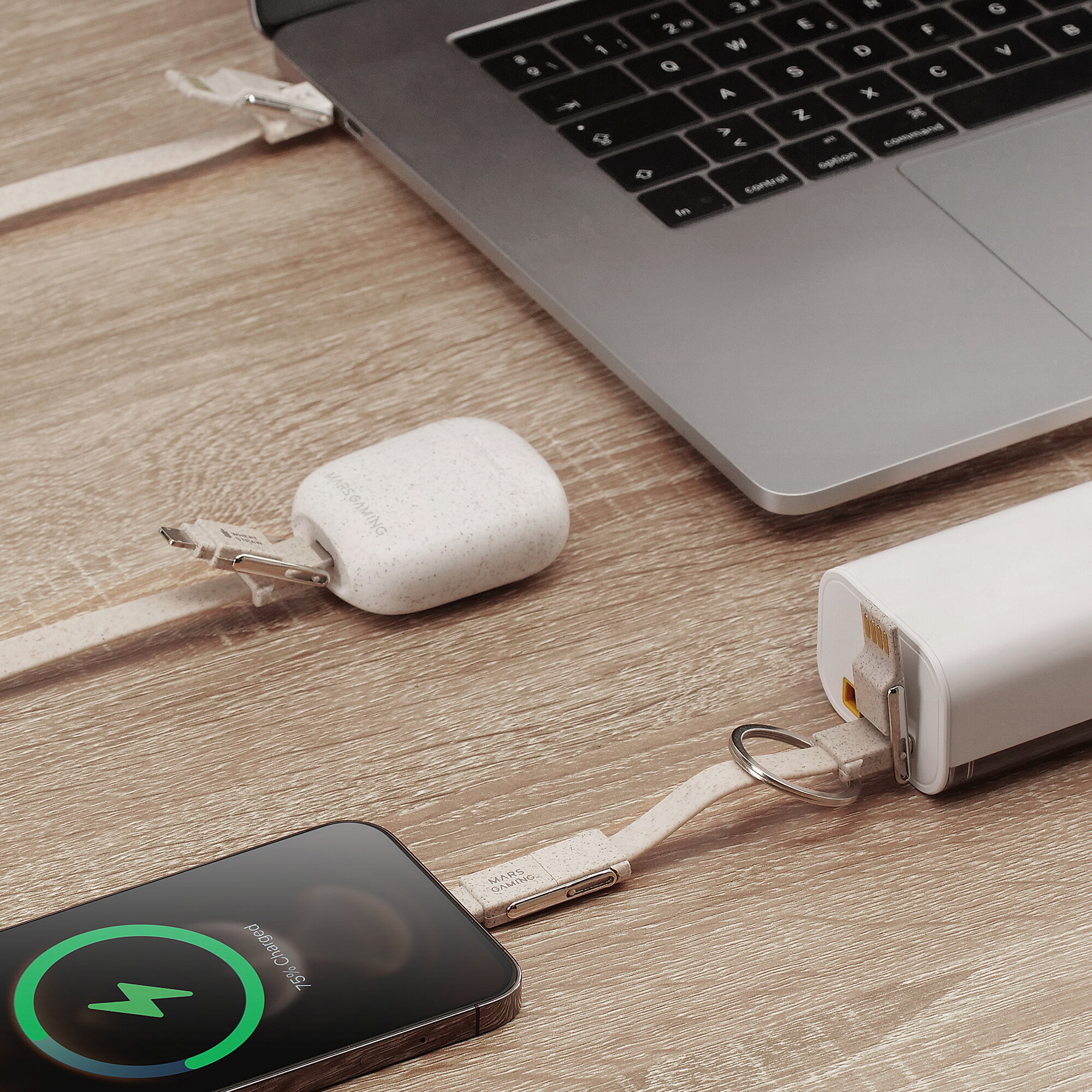 Laptop charging with cable connected to a phone and a power bank on a wooden desk.