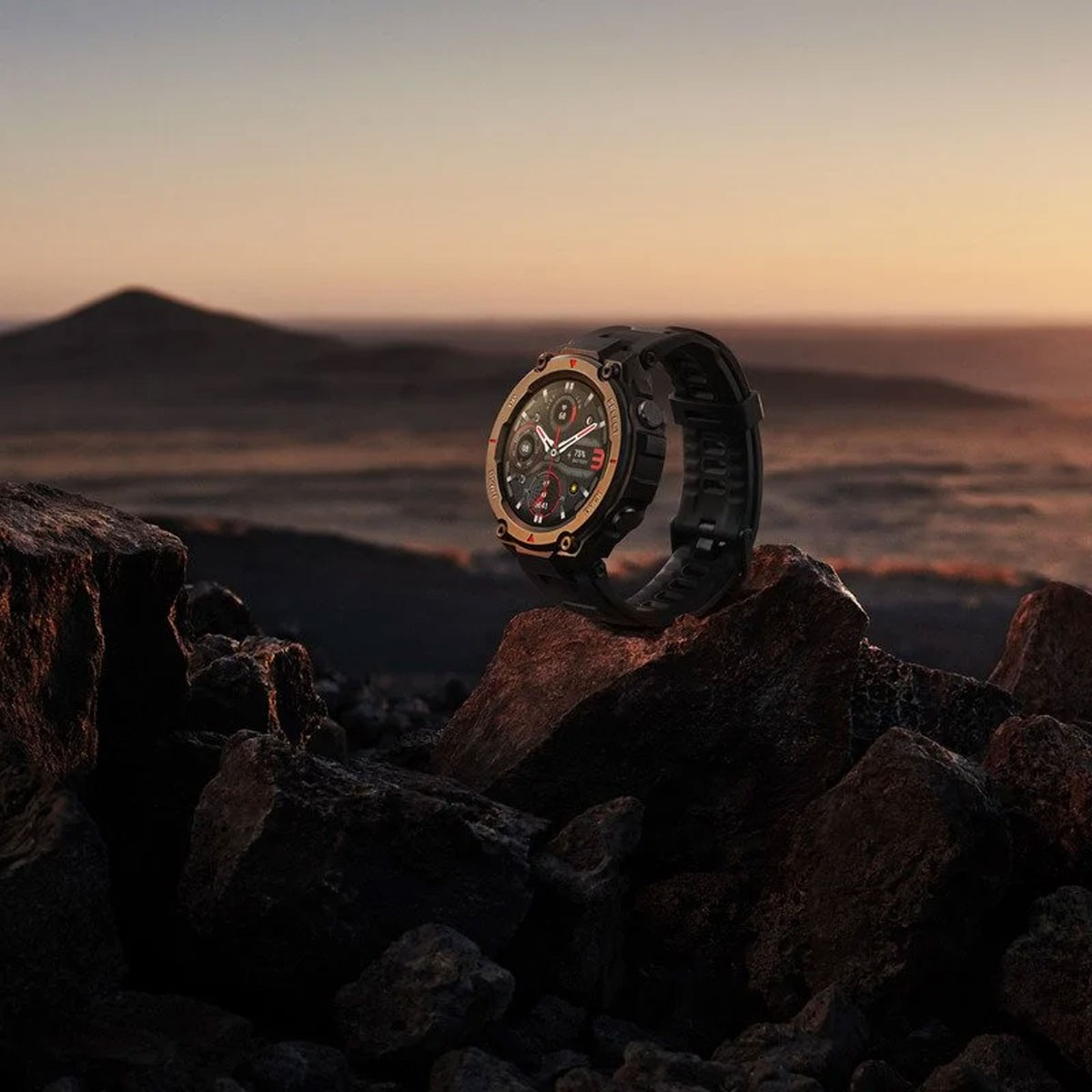 Schwarze Smartwatch auf Felsen, mit einem Gebirge im Hintergrund bei Sonnenuntergang.