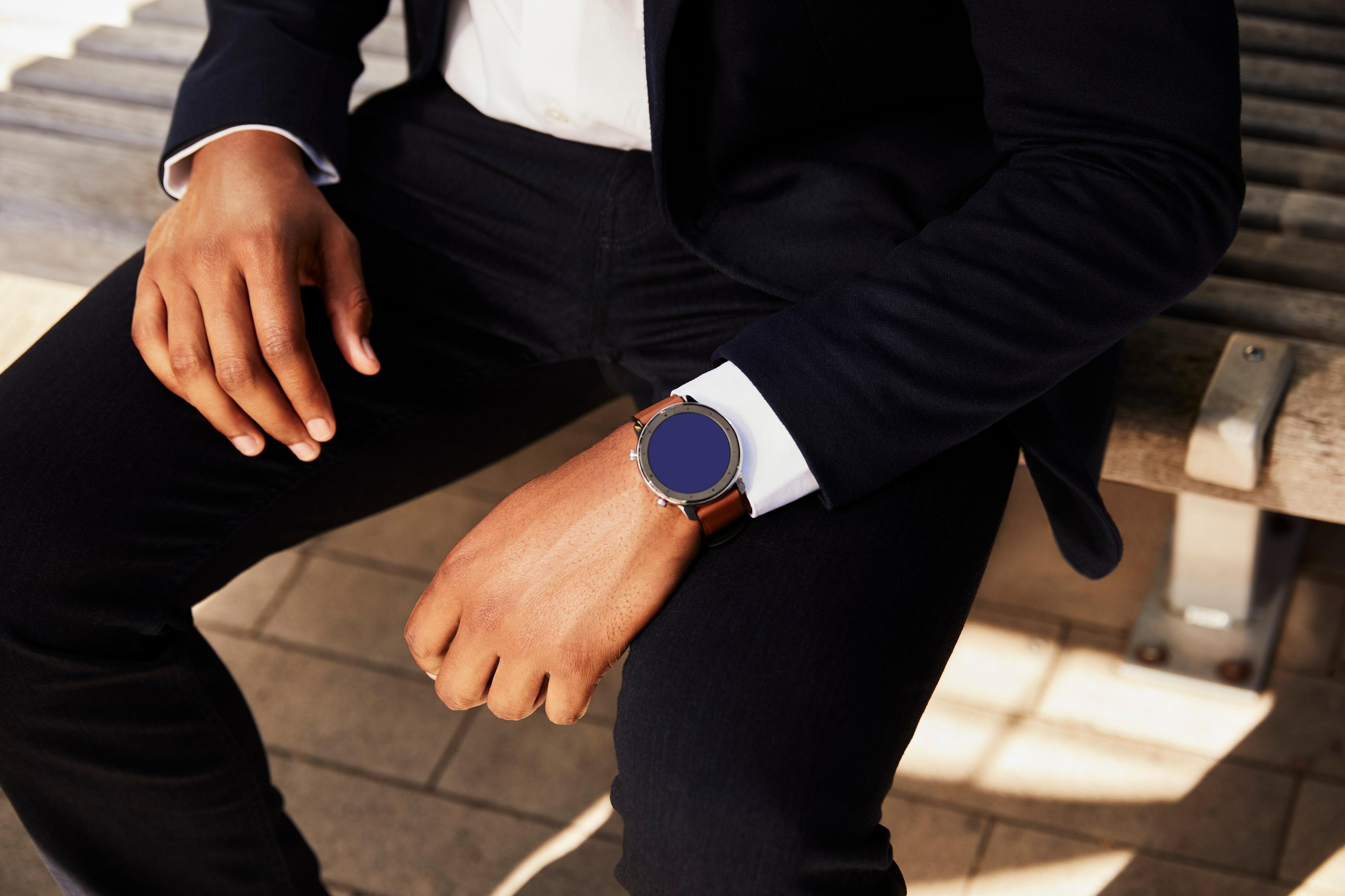 Nahaufnahme eines Mannes mit Smartwatch am Handgelenk, auf einer Holzbank sitzend.