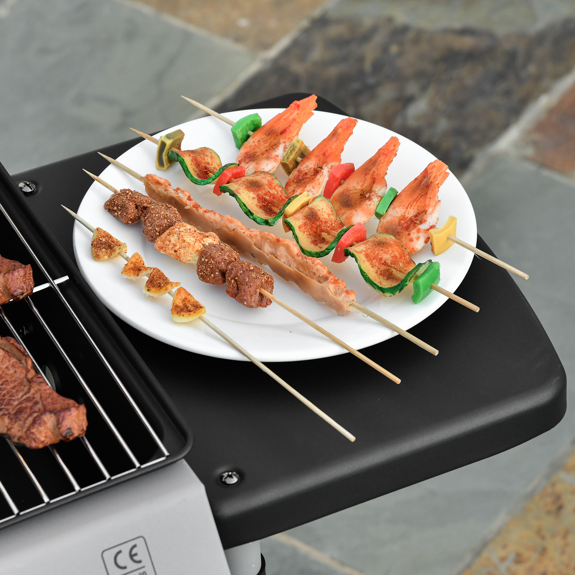 Plato con brochetas a la parrilla. Incluye carne, camarones, verduras. Colocado sobre una superficie negra.