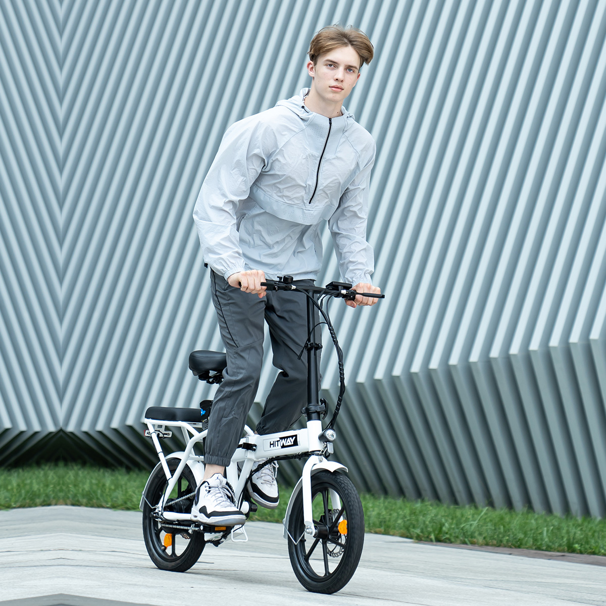 Mann fährt mit einem weißen E-Bike auf einem Bürgersteig neben einem Gebäude.