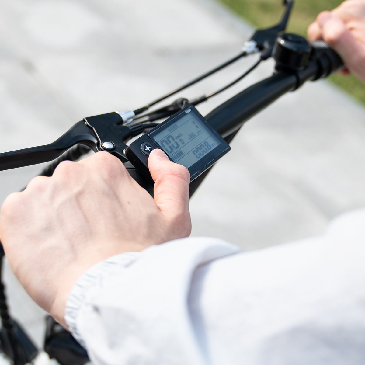 Person passt Fahrradcomputer an. Hintergrund ist Bürgersteig und Gras.