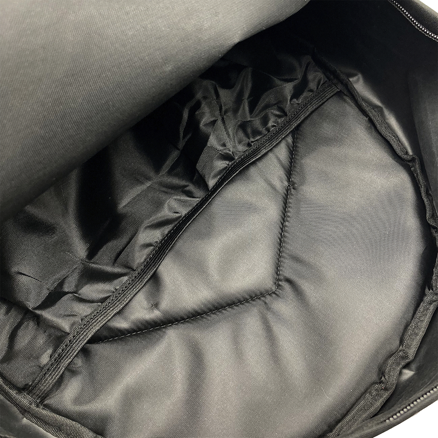 Interior de mochila negra abierta. Visible un bolsillo con cremallera y forro acolchado.
