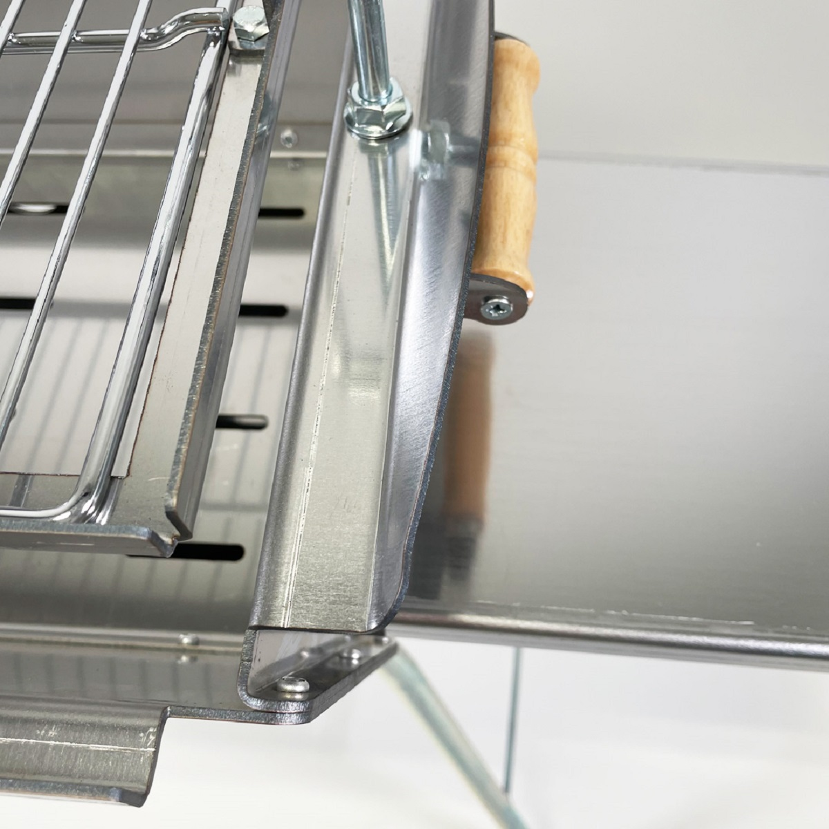 Nahaufnahme eines Metallgrills. Der Grill befindet sich auf einem Metallrahmen mit Holzgriff.