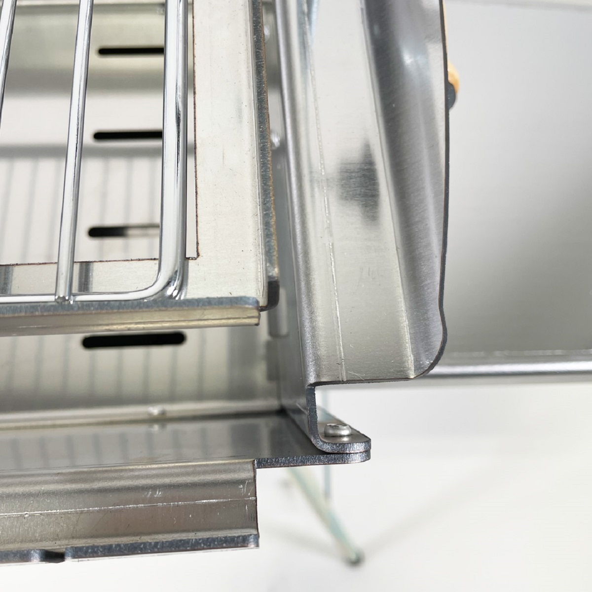Nahaufnahme eines Metallgitters und -rahmens, möglicherweise Teil eines Grills oder einer Maschine. Glänzende Metalloberflächen sind sichtbar.