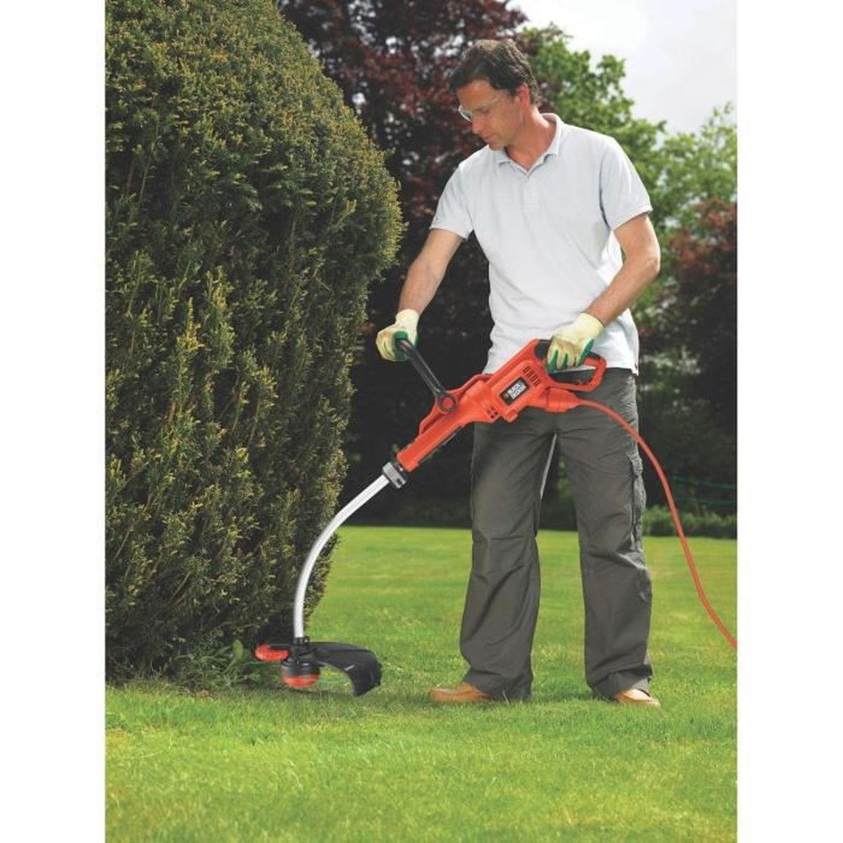 Un hombre usando un cortacésped para cortar césped cerca de un arbusto en un jardín.