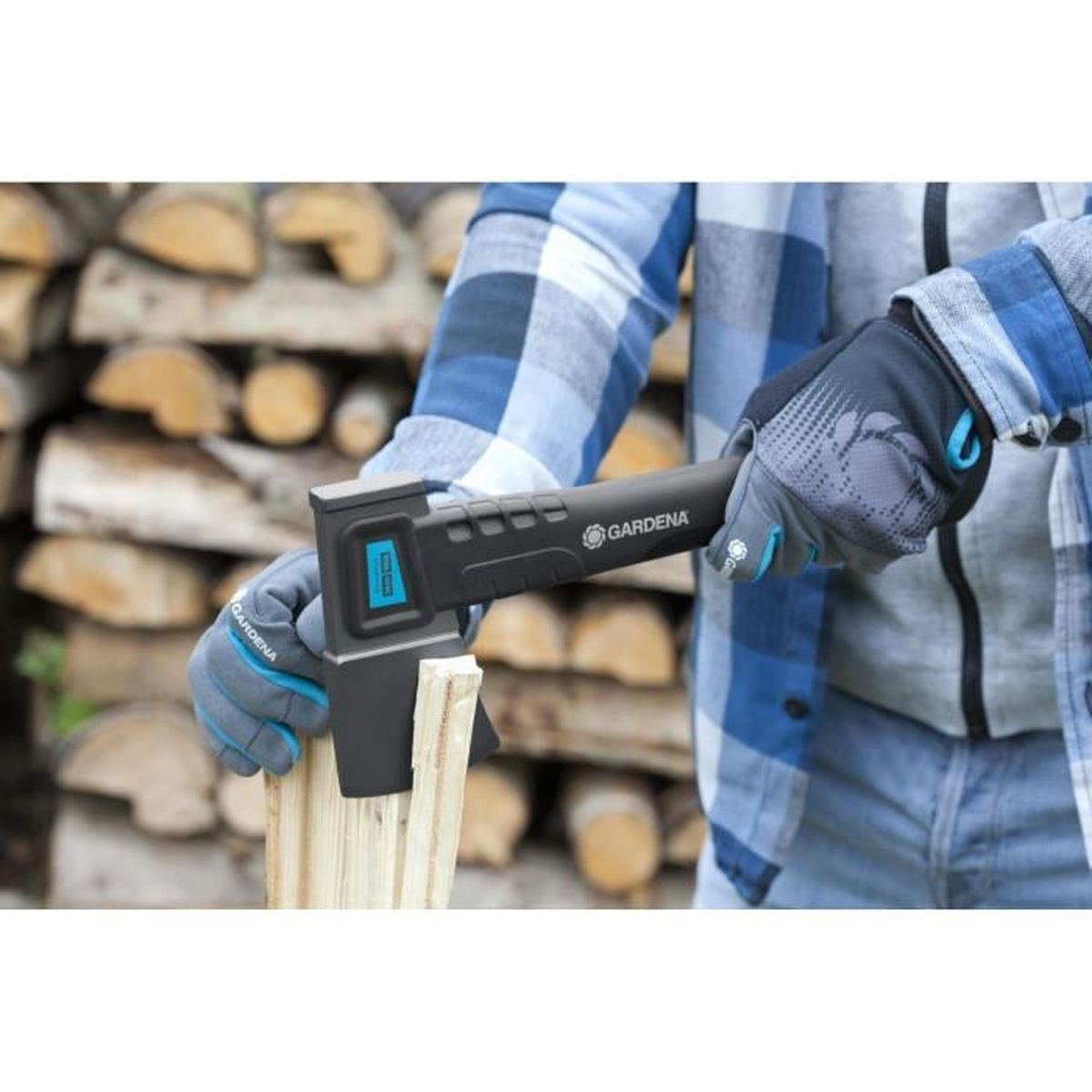 Osoba rąbie drewno siekierą. Siekiera jest czarno-szara. Drewno jest ułożone w tle.