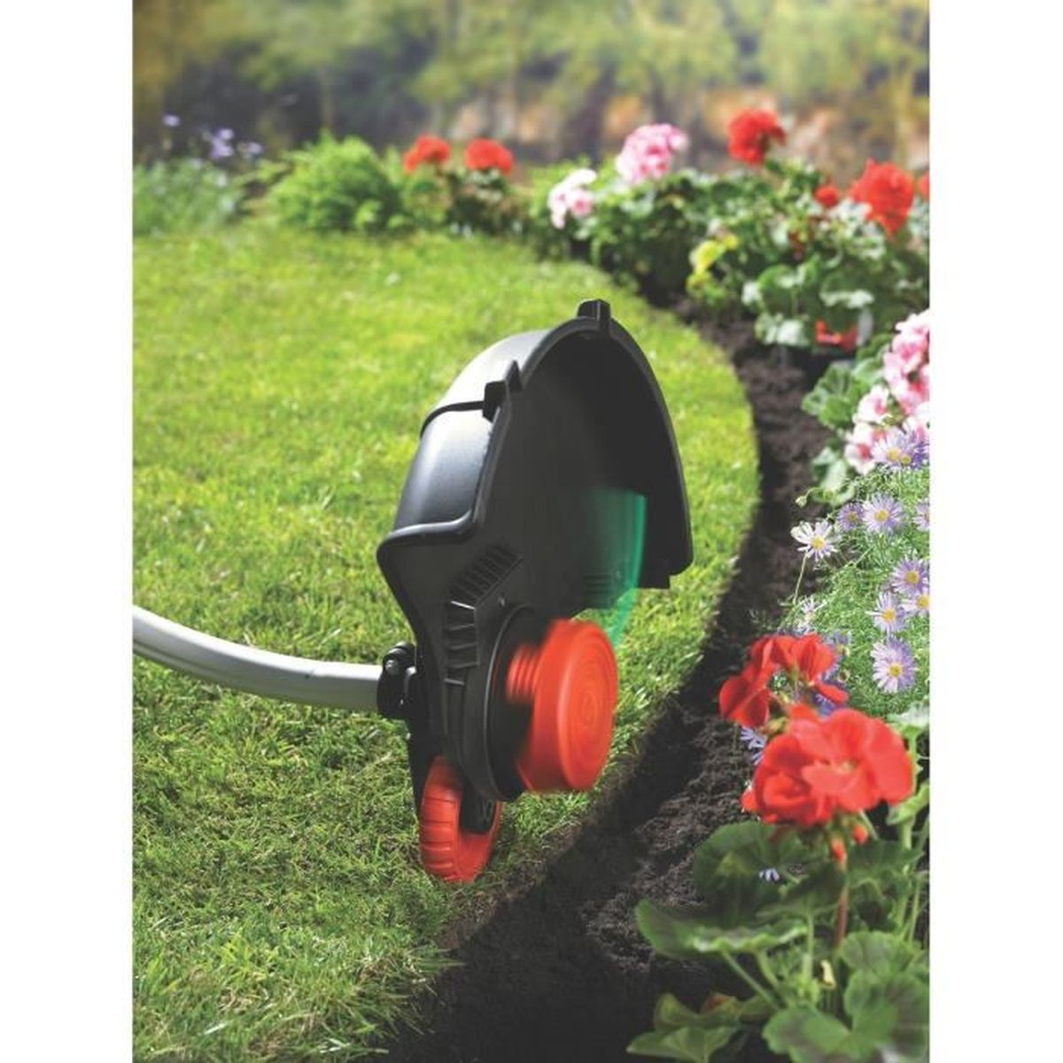 Una herramienta de bordes negra en un jardín con hierba verde y flores rojas en el fondo.