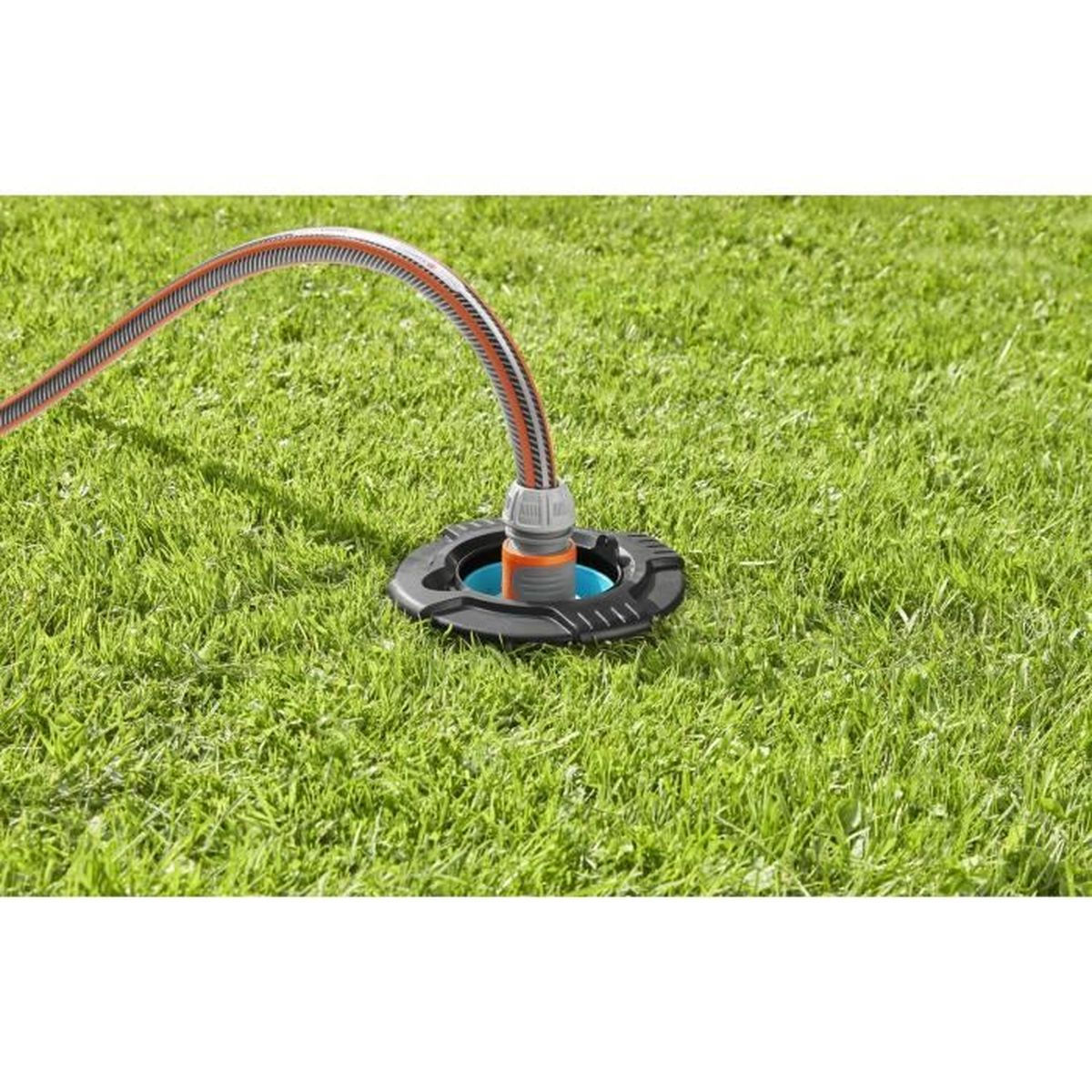 Un irrigatore collegato a un tubo flessibile, posto su erba verde. La testa ha una base nera.