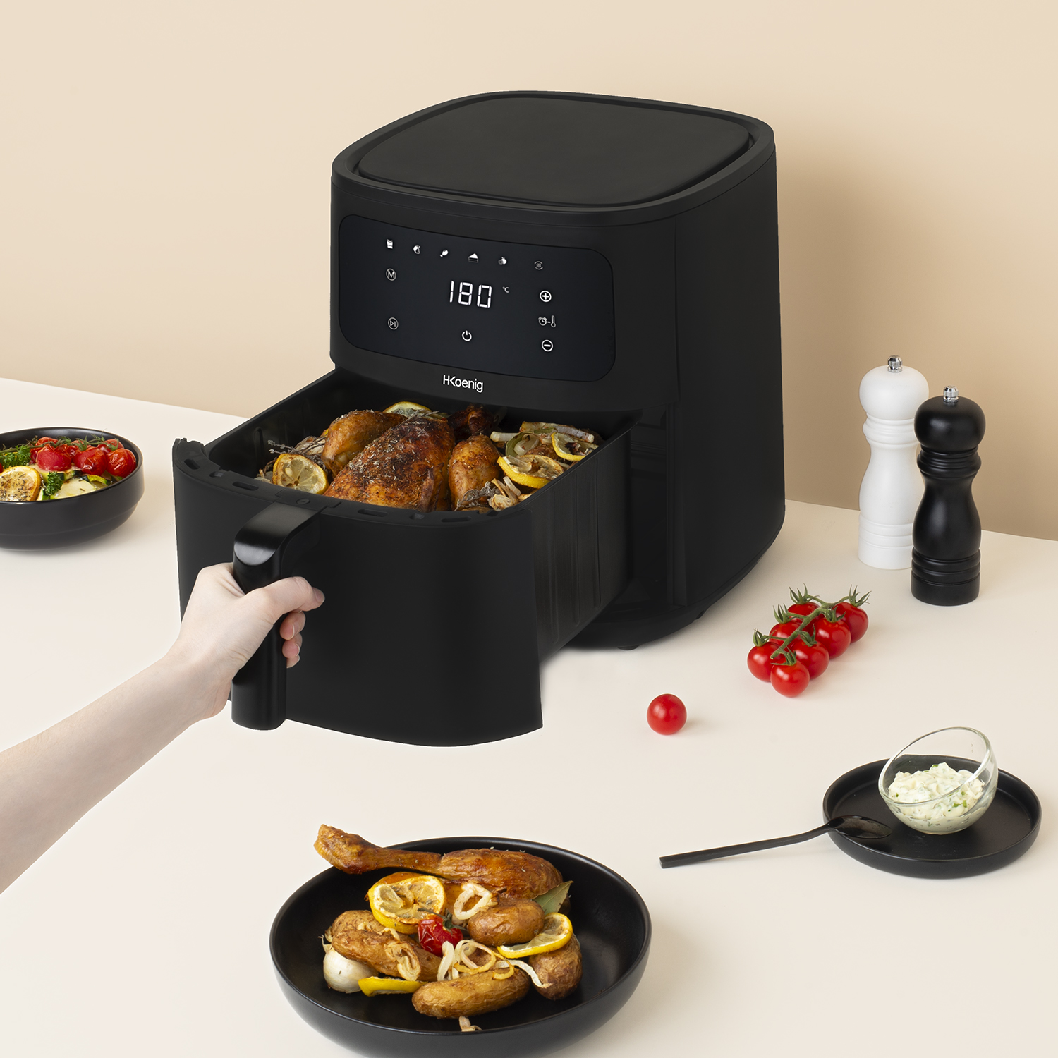 Friggitrice ad aria nera con cibo cotto. Una mano tiene il cestello. Altri alimenti sul tavolo.