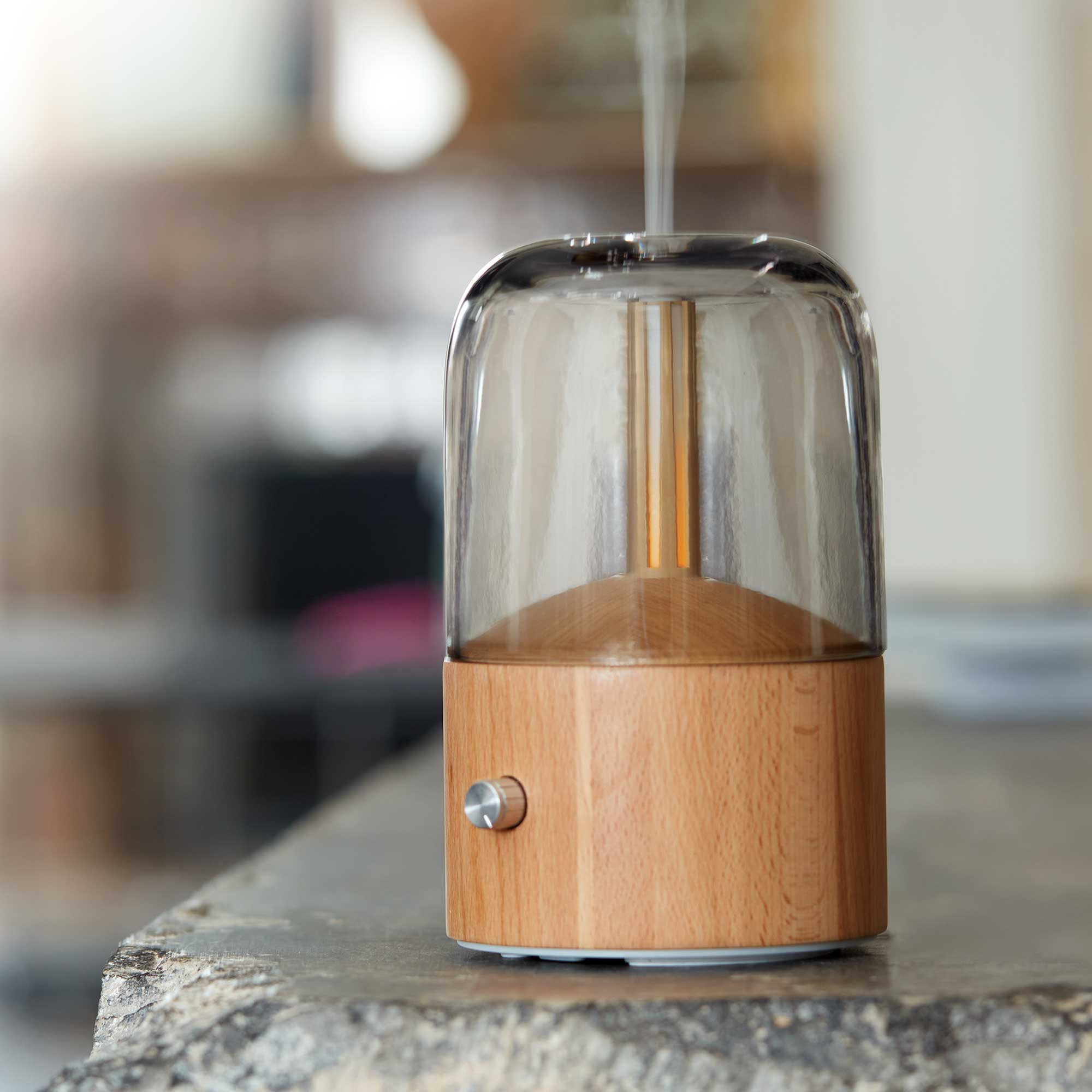 A glass aromatherapy diffuser with a wooden base on a stone surface.