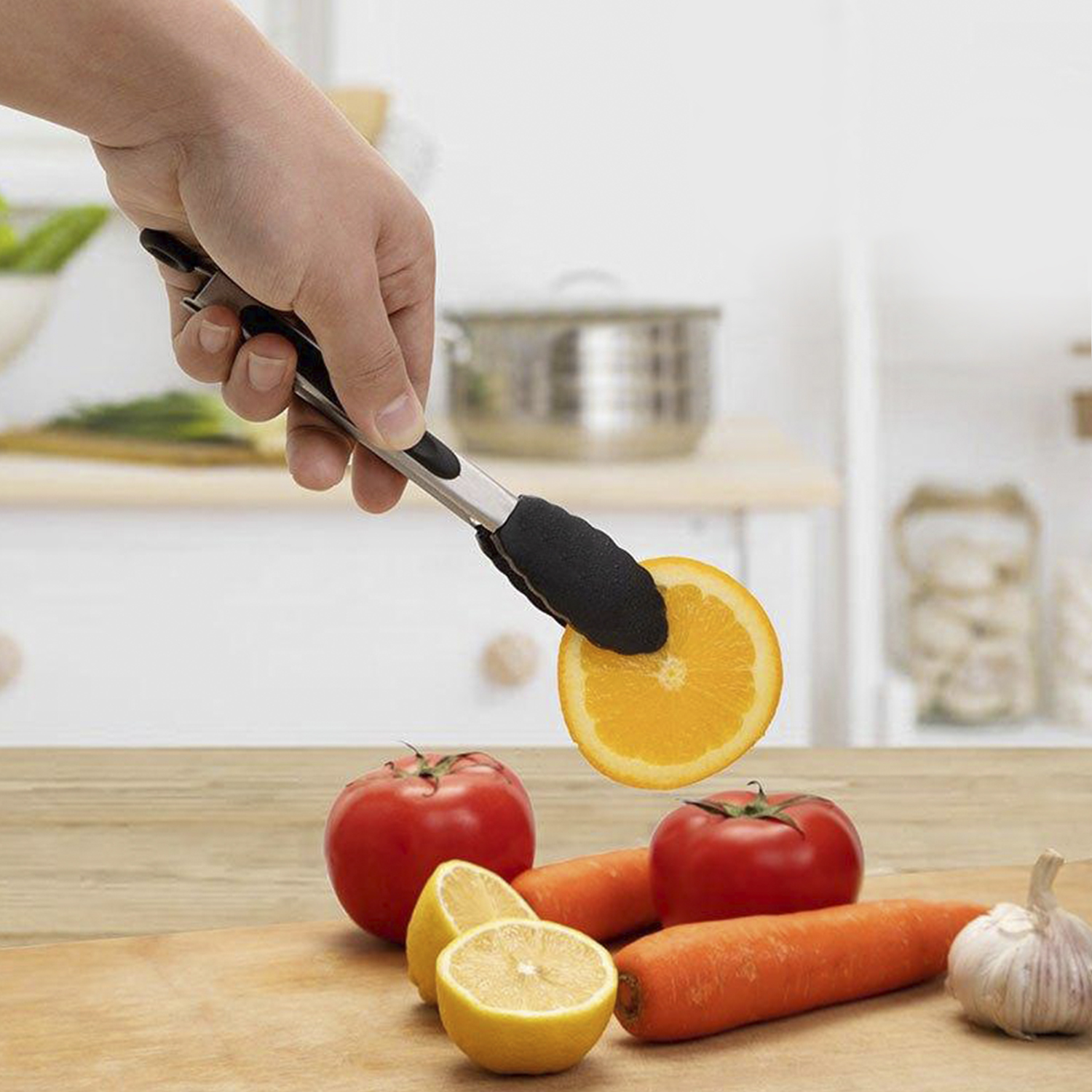 Mano usando pinzas para recoger una rodaja de naranja. Tomates, zanahorias y limón en la tabla de madera.