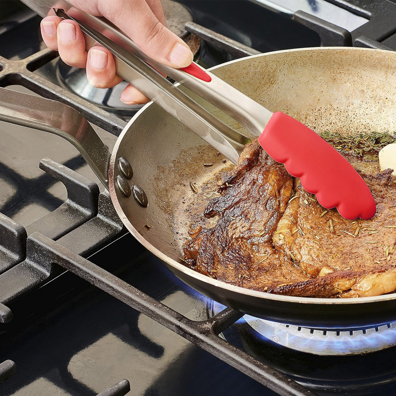 Mano che usa le pinze per girare una bistecca in una padella su un fornello a gas. Silicone rosso sulle pinze.