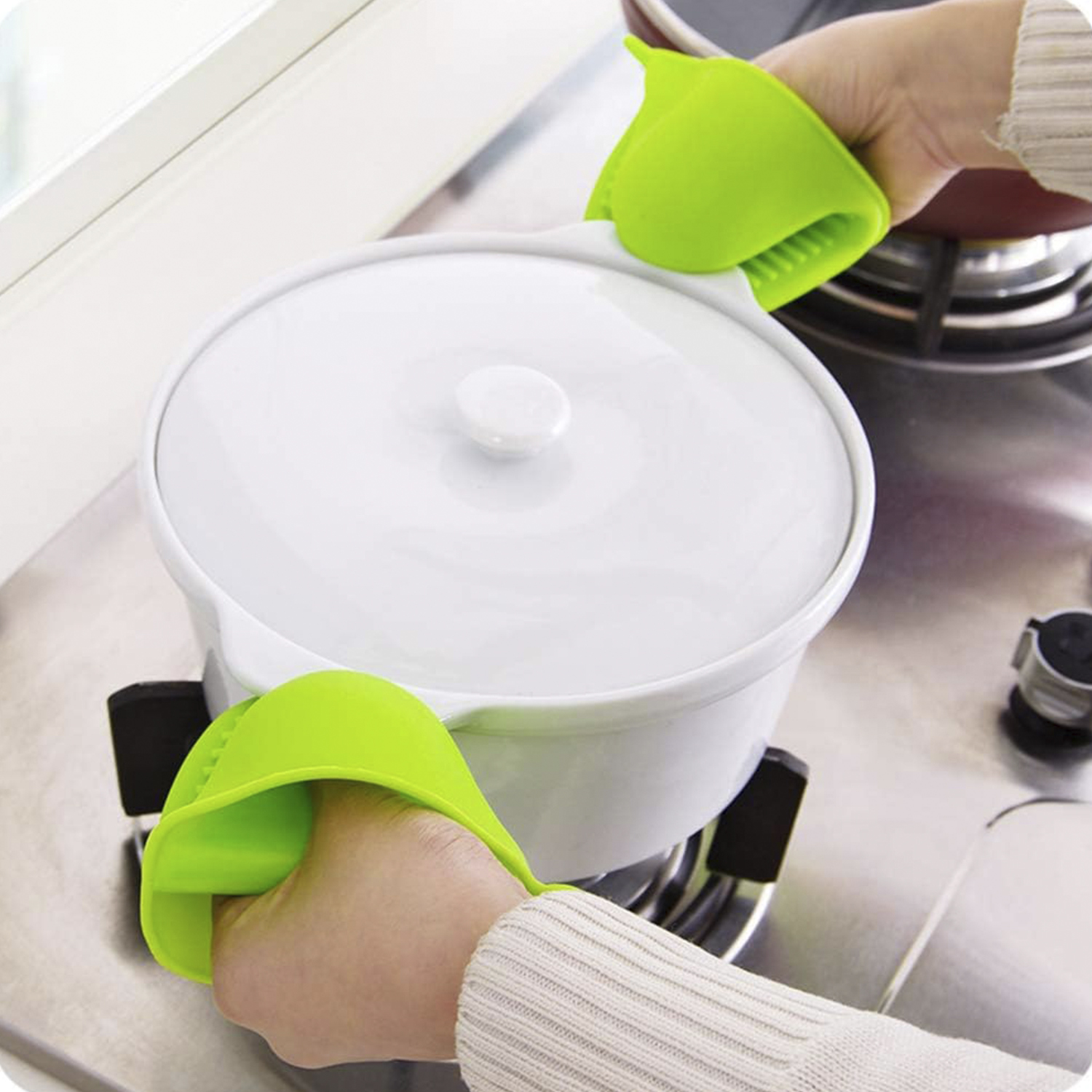 Manos sujetando salvamanteles de silicona verde sobre una olla blanca en la estufa.