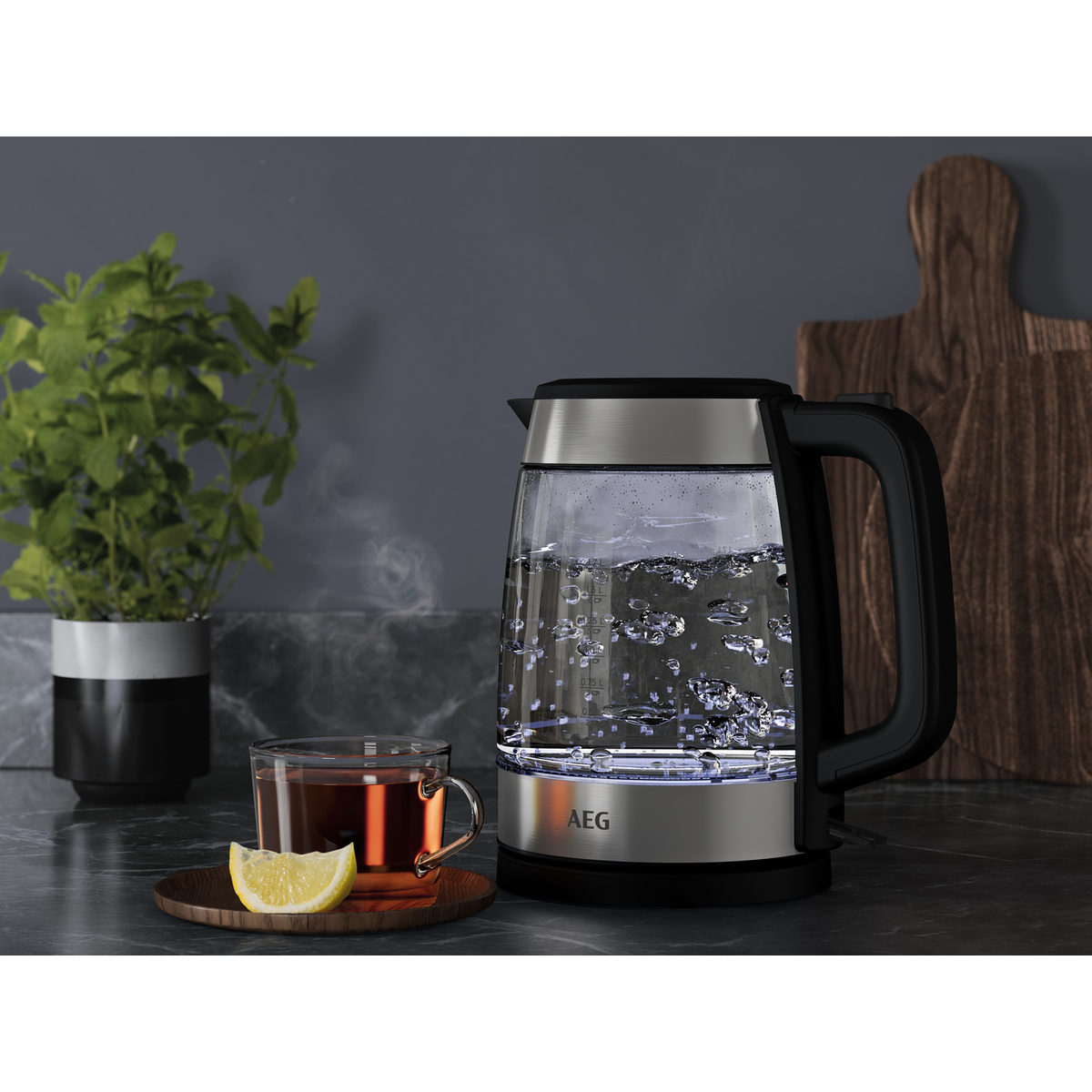 Glaskessel mit kochendem Wasser neben Tee, Zitrone und einem Holzbrett auf der Theke.
