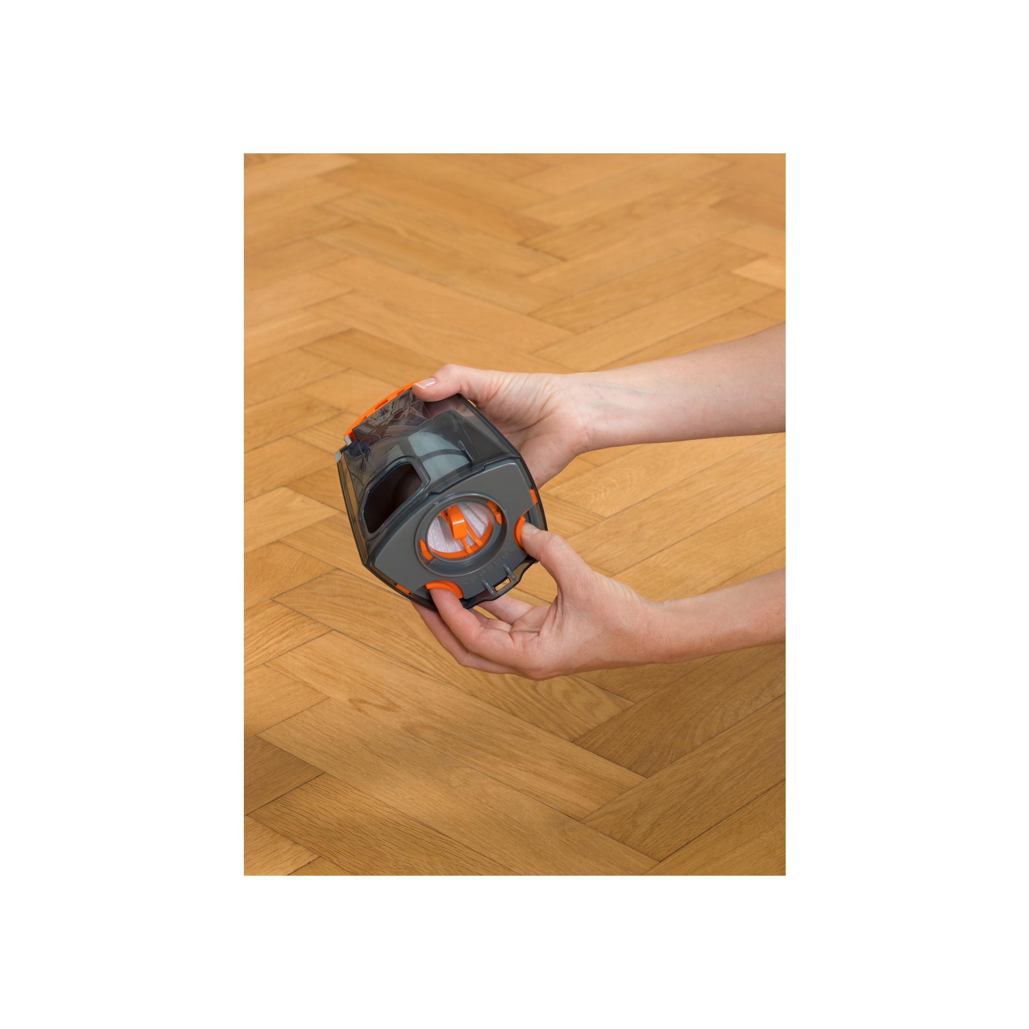 Manos sosteniendo un cubo de basura negro de aspiradora y desenroscándolo contra un fondo de piso de madera.