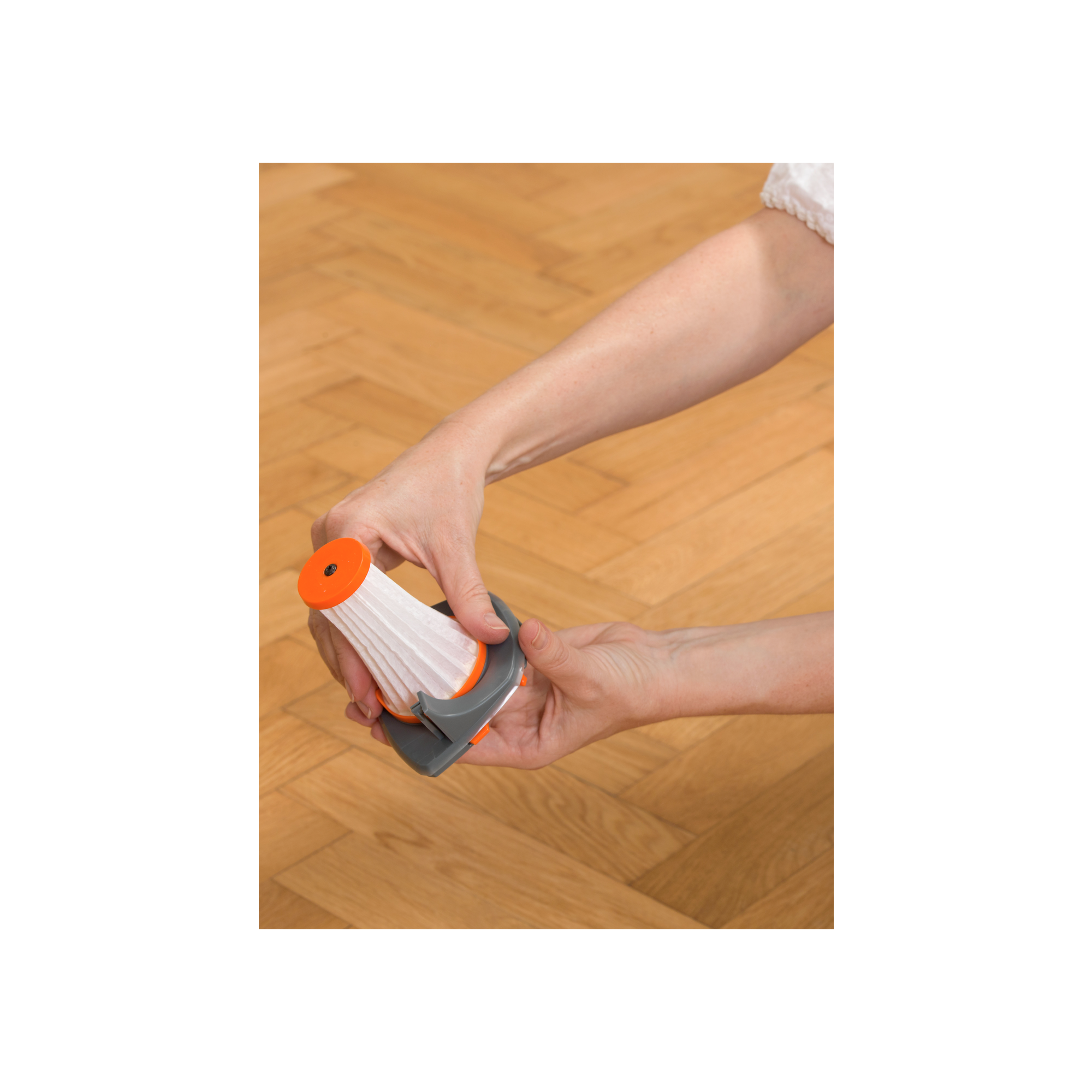 Manos quitando un filtro blanco de un dispositivo gris y naranja, en un suelo de madera.