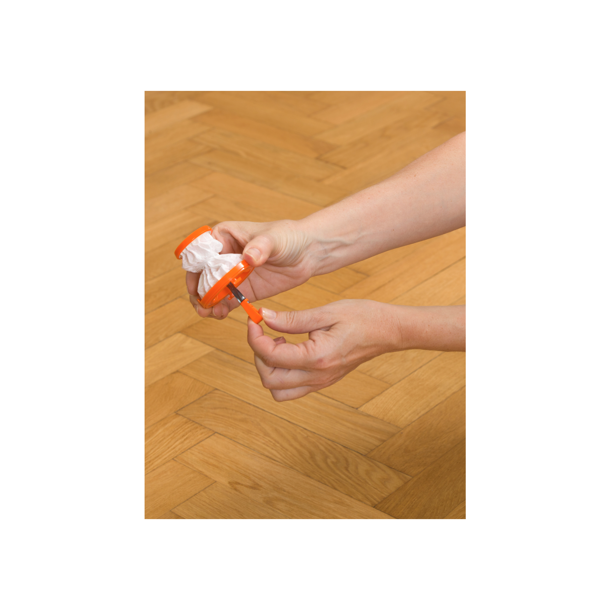 Manos sosteniendo una herramienta naranja con papel blanco en el medio. Fondo de suelo de madera.