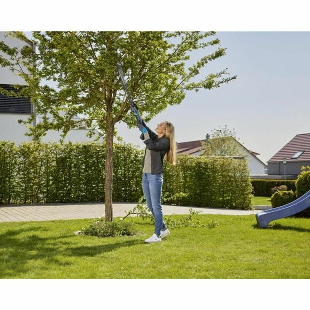 Frau schneidet einen Baum mit einem langen Werkzeug in einem Garten.