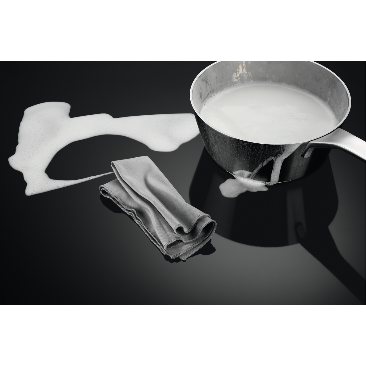 Una olla de leche derramándose sobre una superficie negra. También hay un paño gris.