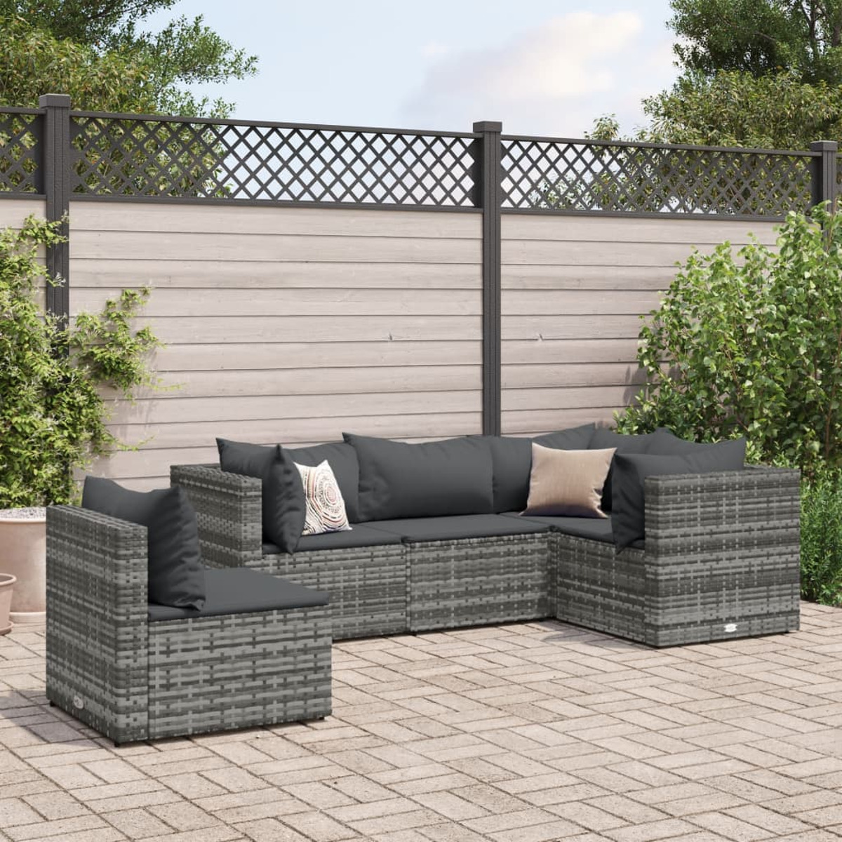 Set di divani in vimini grigio su un patio con cuscini grigi, piante e recinzione.