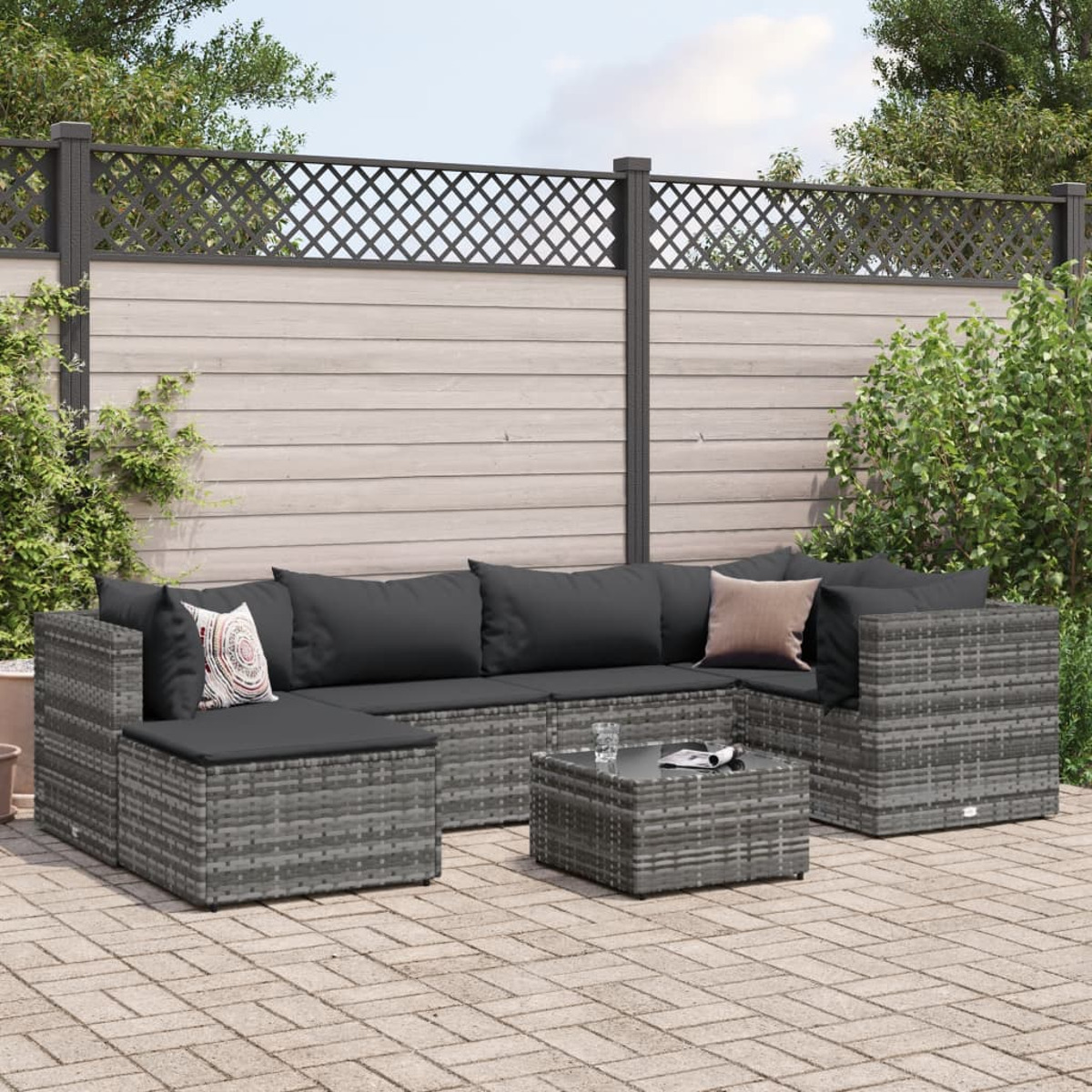 Set patio esterno con divani in vimini grigi, un tavolino e cuscini. Patio in mattoni con una recinzione.