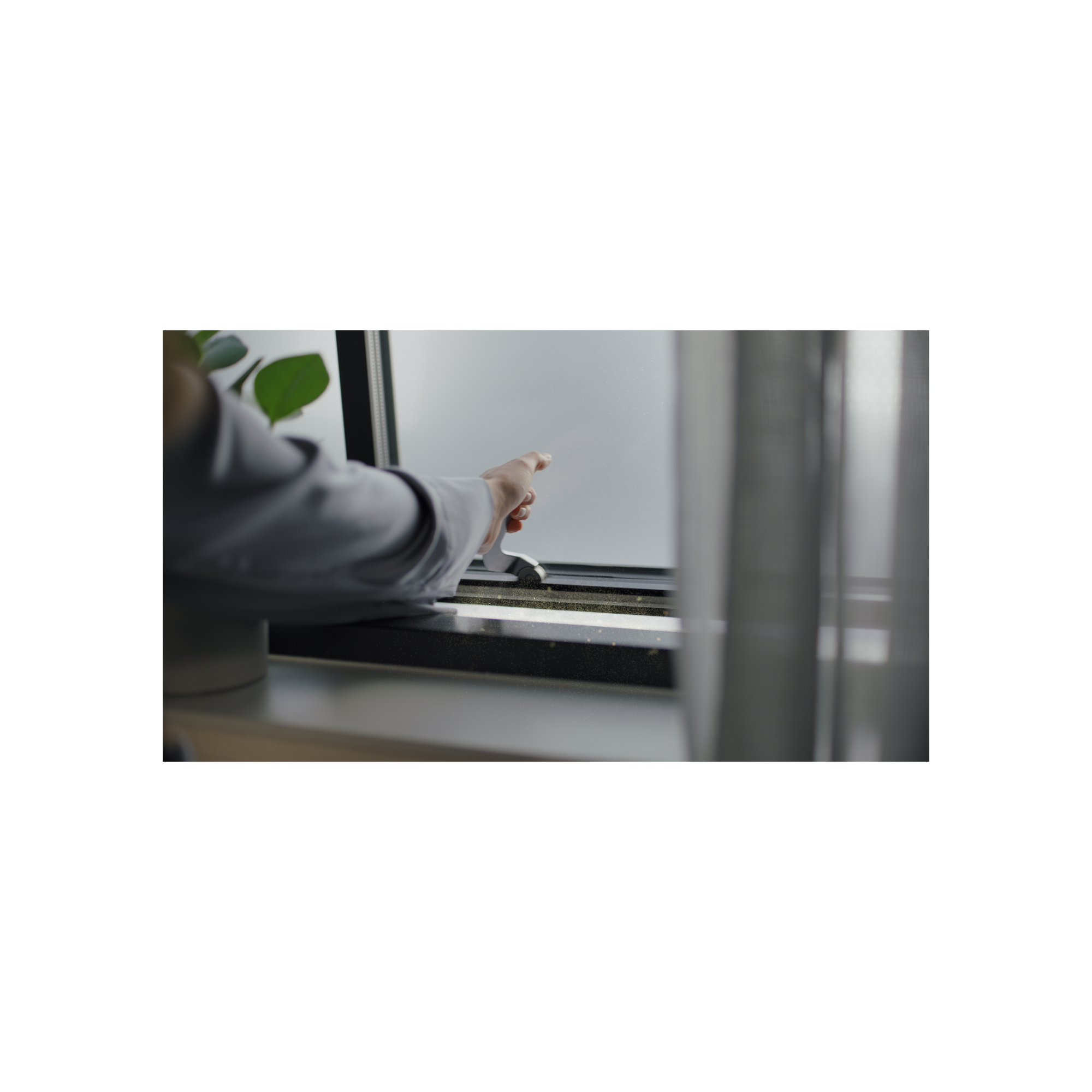 Die Hand einer Person in der Nähe eines Fensterrahmens, mit Vorhang und Pflanzen im Hintergrund.